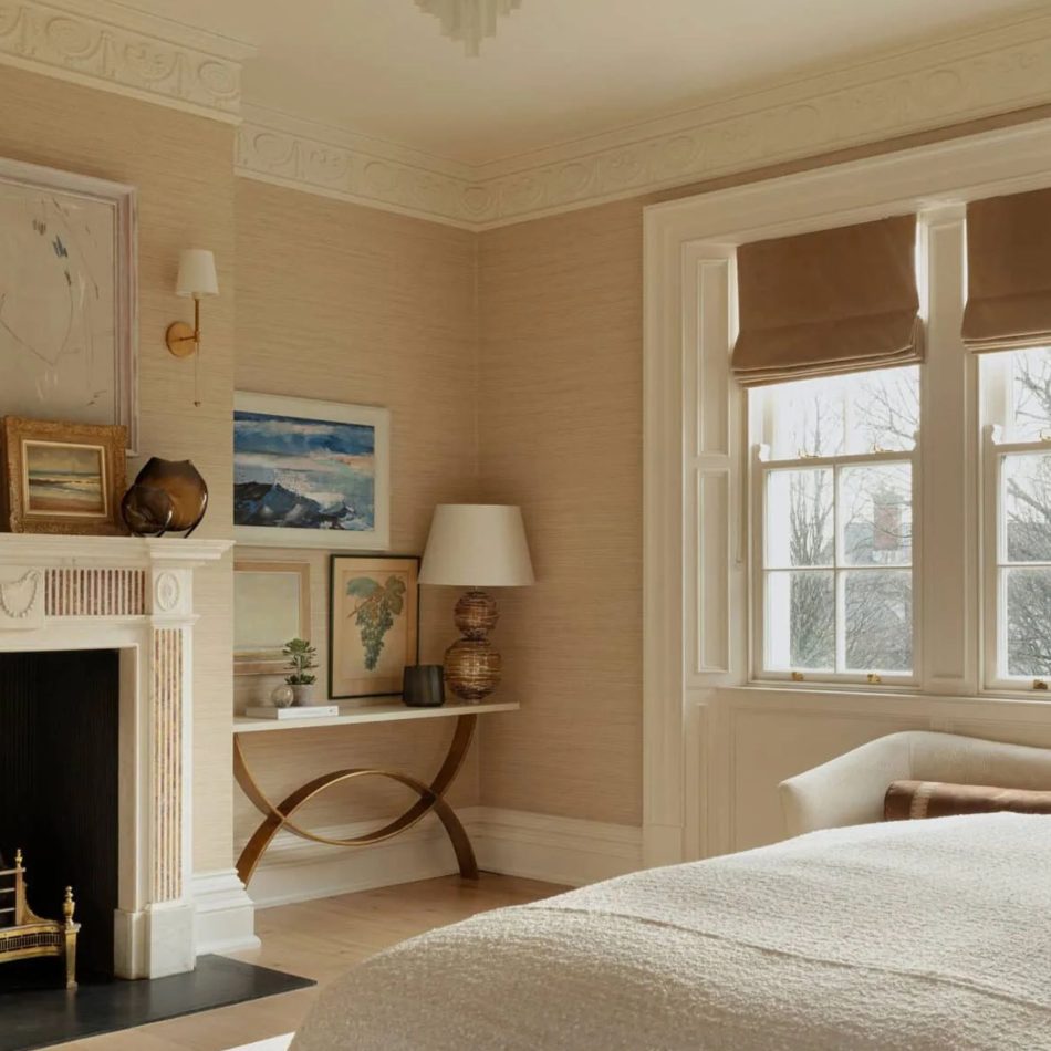 A refined master‑suite corner featuring a white fireplace, abstract artwork, and a console table with gold accents, softly illuminated by natural light from a window with Roman shades. The warm palette and layered textures evoke luxury master bedroom furniture, subtle bedroom architecture, curated design details, and the serene elegance of contemporary furniture within a timeless setting.