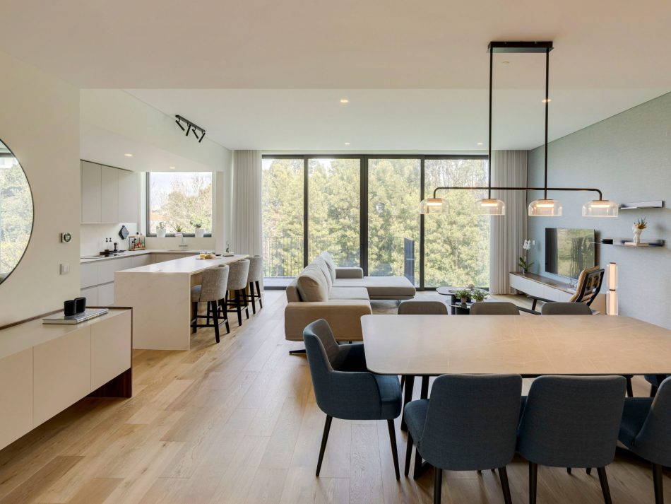 A fluid open‑plan layout where kitchen, dining, and living areas connect effortlessly, anchored by soft neutrals and warm wood textures. The Sky Dining Table and blue seating define the dining zone, while the living area is framed by the Landform TV cabinet and contemporary décor. This cohesive environment reflects refined living room inspiration, elevated by luxury dining room furniture, modern kitchen furniture, and a harmonious palette across all rooms.