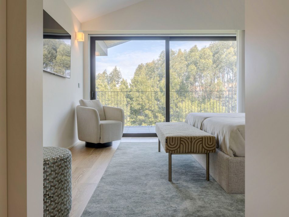 A serene master suite filled with natural light, where the Her Armchair sits beside the window creating a quiet moment of pause. The bed and patterned Sublime Stool introduce soft textures that enhance the calm atmosphere. Warm materials and gentle tones reflect luxury master bedroom furniture, while the overall composition showcases elegant bedroom architecture, subtle wood texture, and refined sophisticated bedroom furniture.