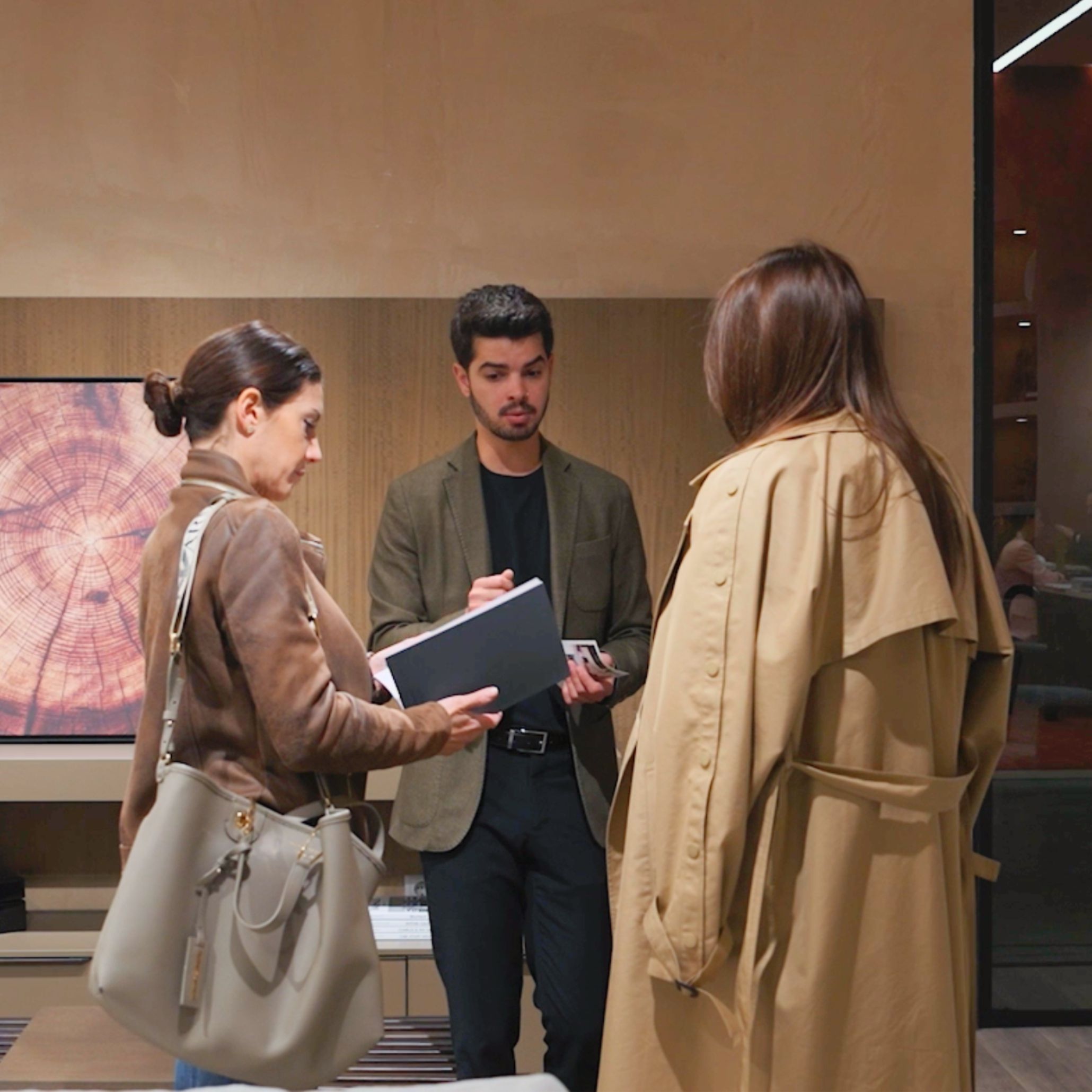 A Stylish Club team member meets with clients inside a warm, modern stand , discussing ideas shaped by the evolving influence of Milan Design Week 2026. The setting reflects a shift toward intentional design, where natural materials and thoughtful details guide conversations around luxury furniture, inspire new directions in interior design inspiration, and highlight the growing importance of authenticity in modern furniture.