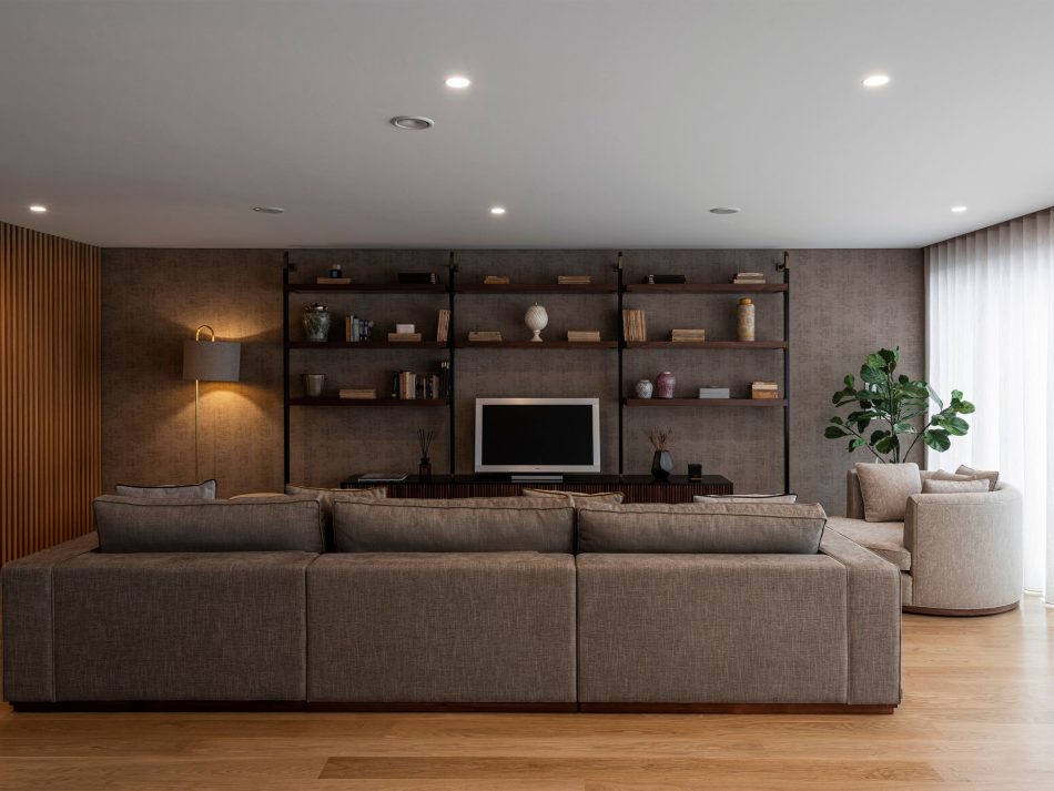 A spacious living room where the Fortune Sofa introduces a quiet, inviting presence with its aligned upholstery and matt walnut base, while the Empire Armchair adds sculptural contrast through its rotating form. Along the wall, the Bespoke Ryan TV Cabinet grounds the space with refined luxury furniture craftsmanship, as soft textures and warm wood finishes create a sense of modern design harmony and understated sophistication.
