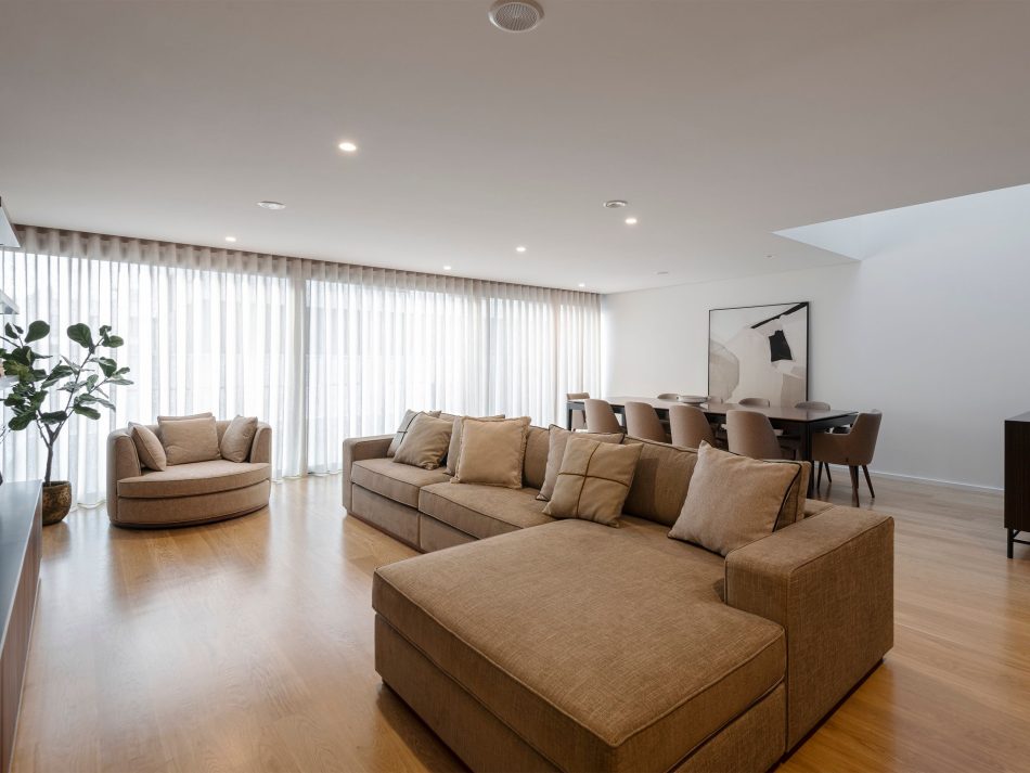 A bright, expansive living space where the Empire Armchair introduces a sculptural presence, its soft curves adding personality to the room. Natural light filters through sheer curtains, softening the textures and enhancing the calm openness of the space, which is shaped by modern furniture, warm materials, and the understated elegance of contemporary living.