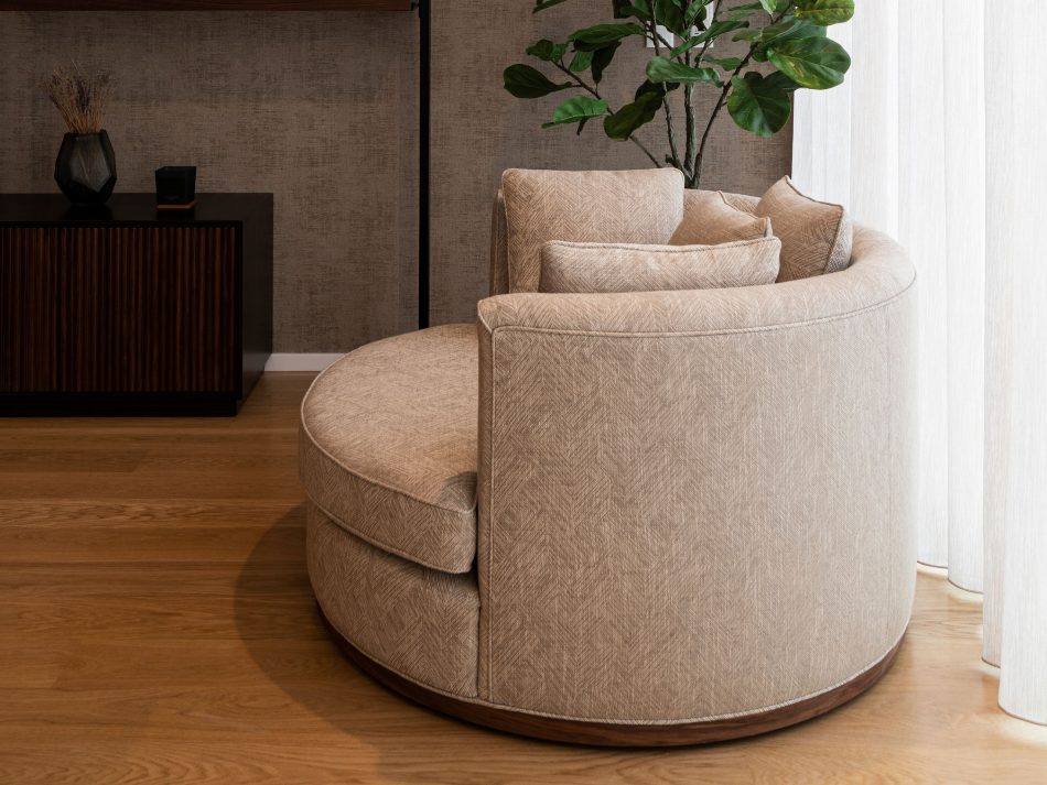 A quiet corner of the living space featuring the Empire Armchair, its curved form and textured upholstery bringing a gentle sense of comfort. Natural light and simple materials contribute to a refined setting defined by modern furniture and a clean, elegant layout.
