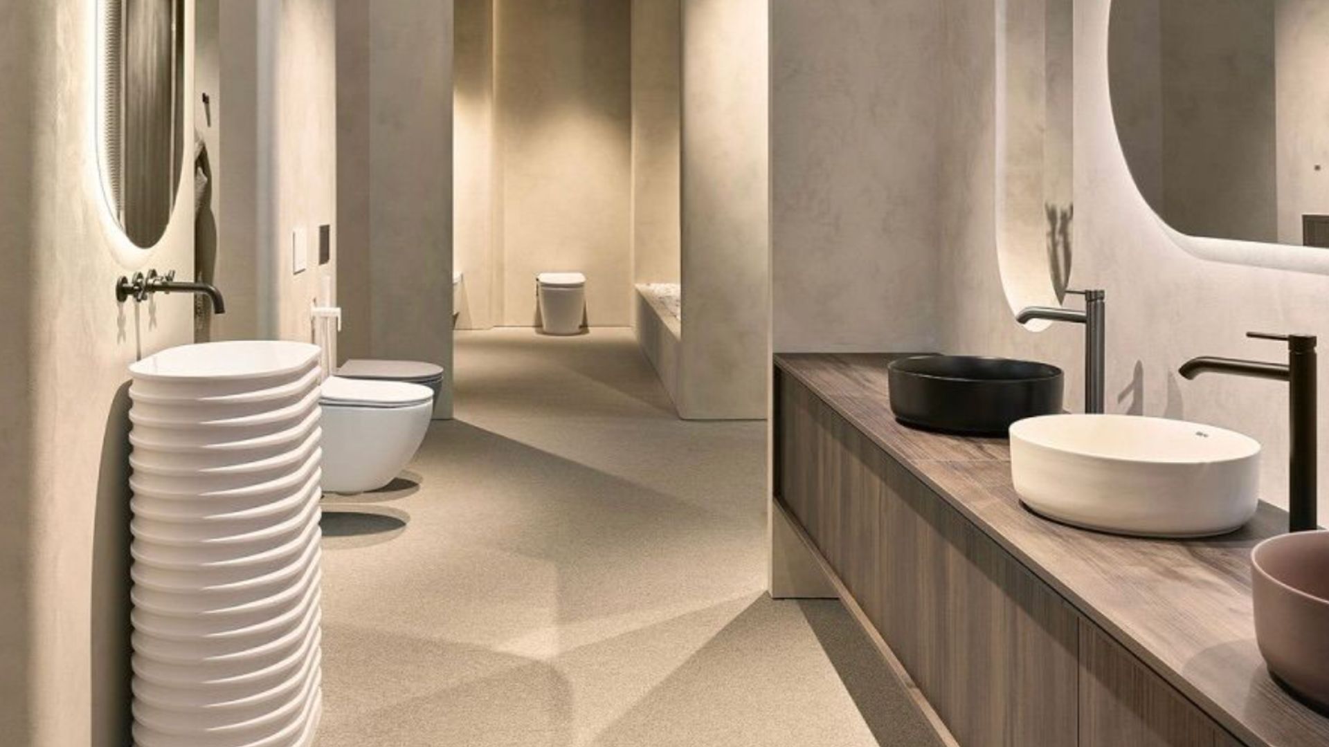 Visitors explore a contemporary bathroom installation at the International Bathroom Exhibition, where sculptural basins, layered textures, and refined fixtures illustrate a new vision of wellness within the home. The display highlights how design influences everyday rituals, bringing attention to detail, atmosphere, and material expression across Salone del Mobile 2026, connected to mirror design and the evolving world of luxury home furniture.