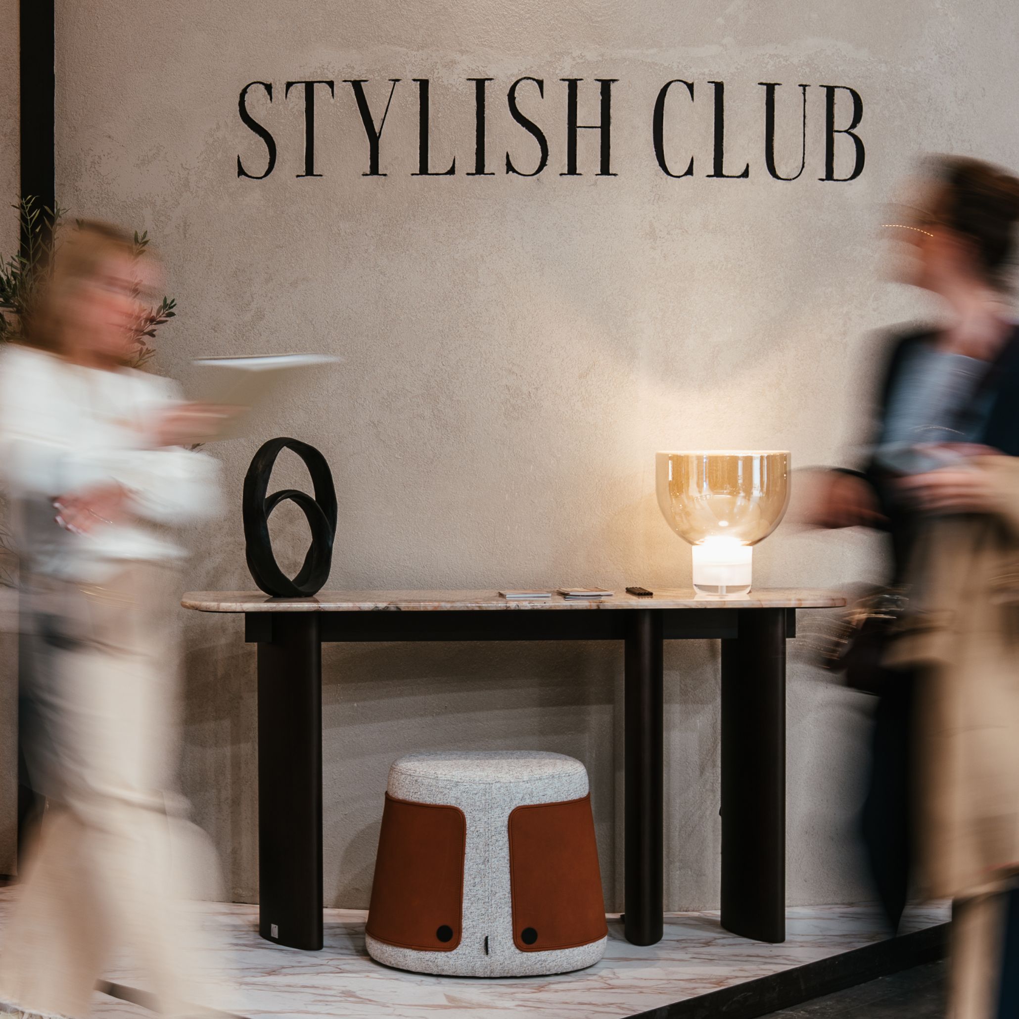 The entrance of the Stylish Club stand reveals soft curves and warm lighting that introduce the elemental concept with a calm, sculptural presence. The architecture blends Parisian influence with contemporary fluidity, offering a first glimpse into luxury home furniture. As visitors pass by, the crafted details highlight the precision of bespoke furniture, while the overall composition sets a serene tone filled with subtle interior design inspiration.