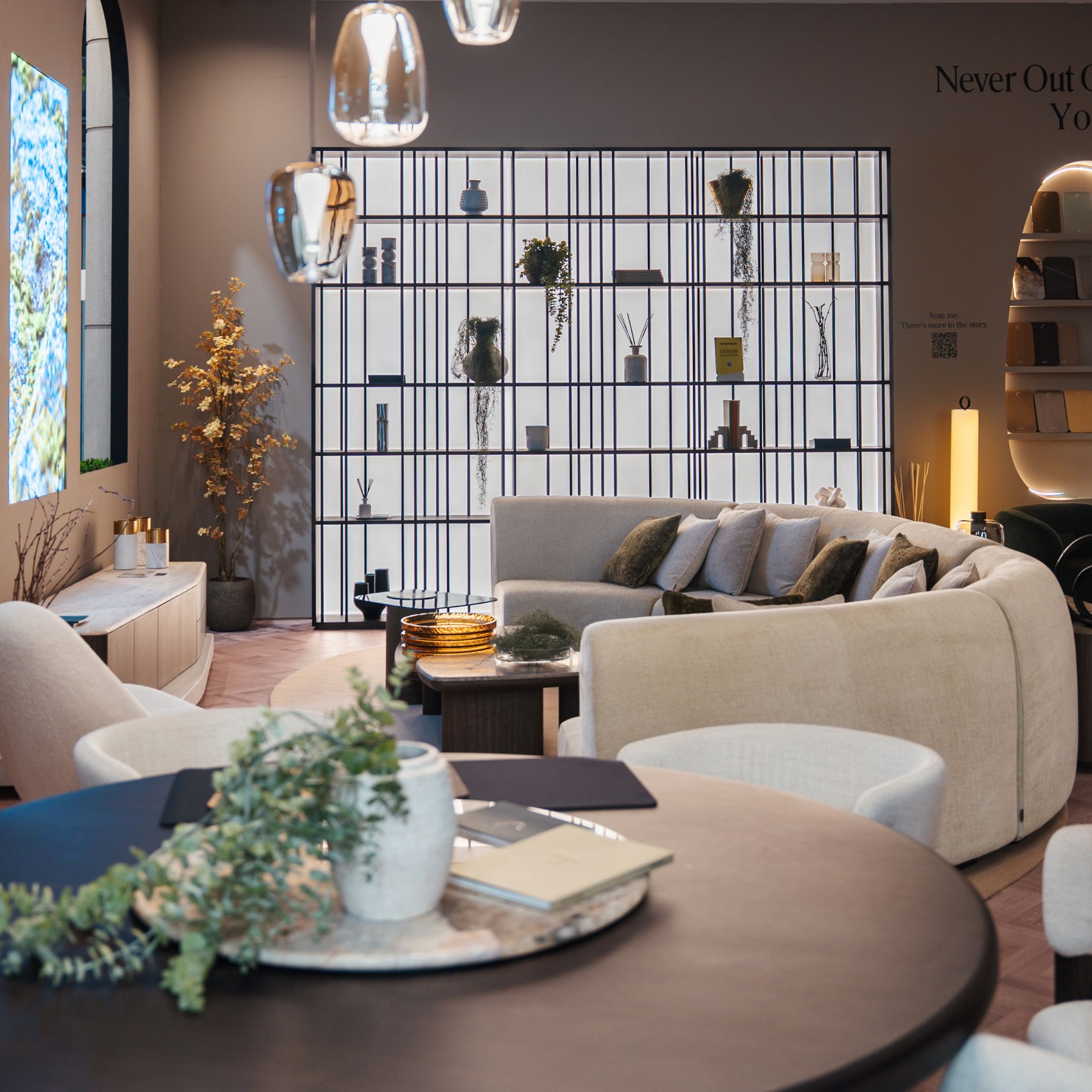 Inside the stand, the living and dining area unfolds as a warm, continuous space shaped by soft curves, layered textures, and ambient lighting. A rounded sofa anchors the room, complemented by sculptural tables and a grid-like shelving structure that guides the eye naturally. The setting reflects a thoughtful approach to living room furniture, enriched by the presence of contemporary furniture and a layout designed to spark living room inspiration.