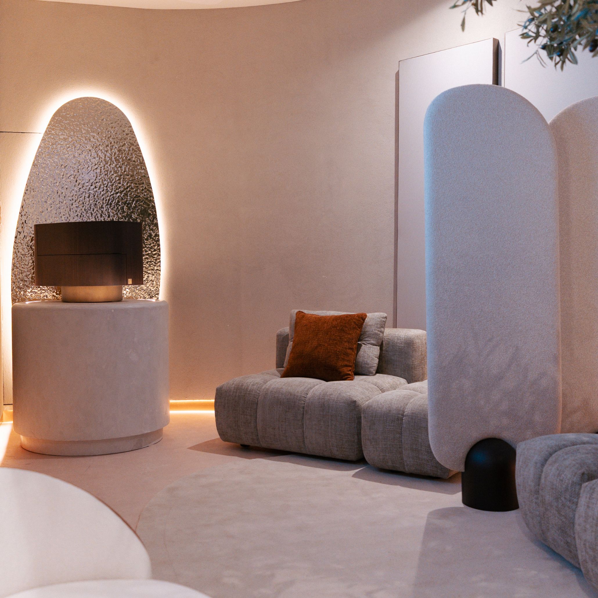 The private area reveals a calm, intimate environment anchored by the Antónia Modular Sofa, whose soft curves and textured upholstery create a welcoming space for quiet meetings. Warm lighting enhances the sculptural pedestal displaying the Stone Night Table II, allowing its details to be appreciated from every angle. The gentle interplay of materials and forms conveys the refinement of luxury furniture, balanced with the quiet elegance of modern furniture and a setting shaped for thoughtful design details.