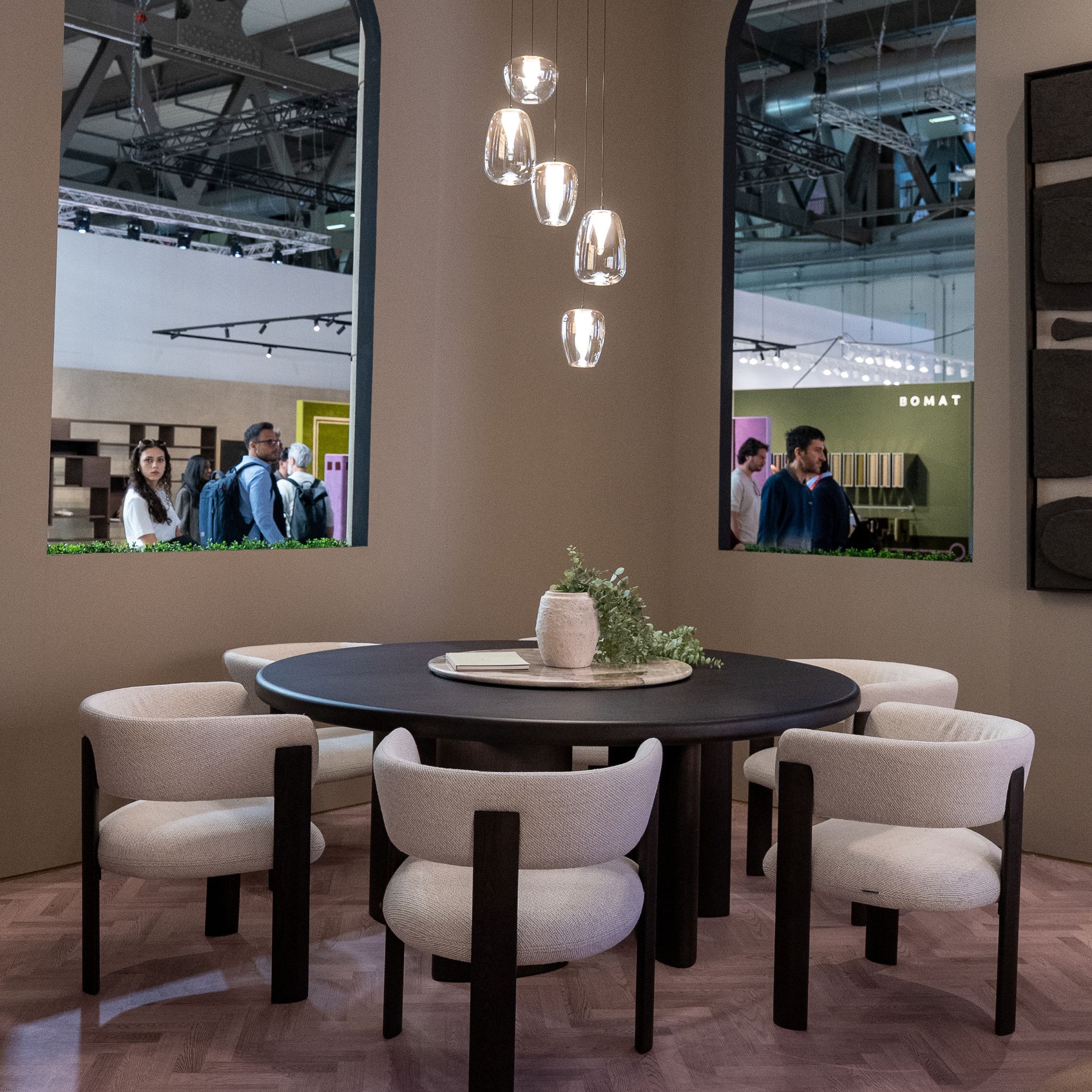 The dining area features the Dolomites Round Dining Table paired with Dolomites Chairs, arranged beneath a cluster of glass pendant lights that cast a warm, inviting glow. The arched openings frame views of the fair, creating a sense of openness while maintaining an intimate dining atmosphere. This setting embodies the elegance of luxury dining room furniture, the sculptural clarity of modern dining table design, and a layout shaped to inspire refined dining room furniture experiences.