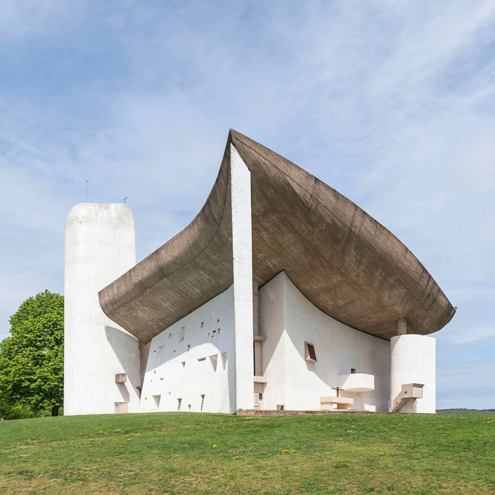 The sculptural exterior of Notre Dame du Haut rises from the hillside with sweeping concrete curves and a floating roof, an expressive composition that continues to inspire luxury furniture through its bold forms, influence high end furniture with its material honesty, and inform design details that celebrate light, texture, and architectural emotion.