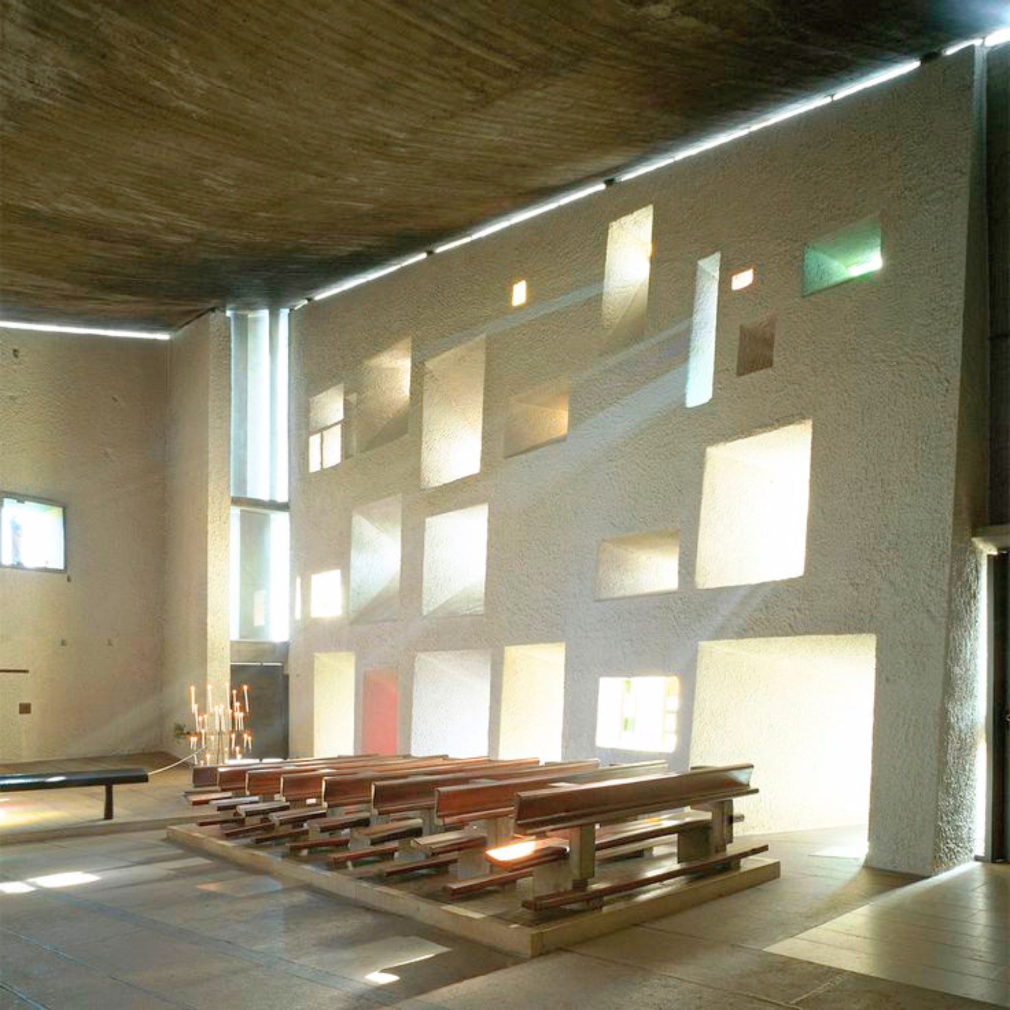 Inside Notre Dame du Haut, beams of natural light filter through sculpted openings, creating a serene atmosphere where Le Corbusier’s interplay of shadow and form echoes the crafted refinement of luxury home furniture, the expressive simplicity found in handmade furniture, and the spatial clarity that guides interior design inspiration in contemporary architecture.
