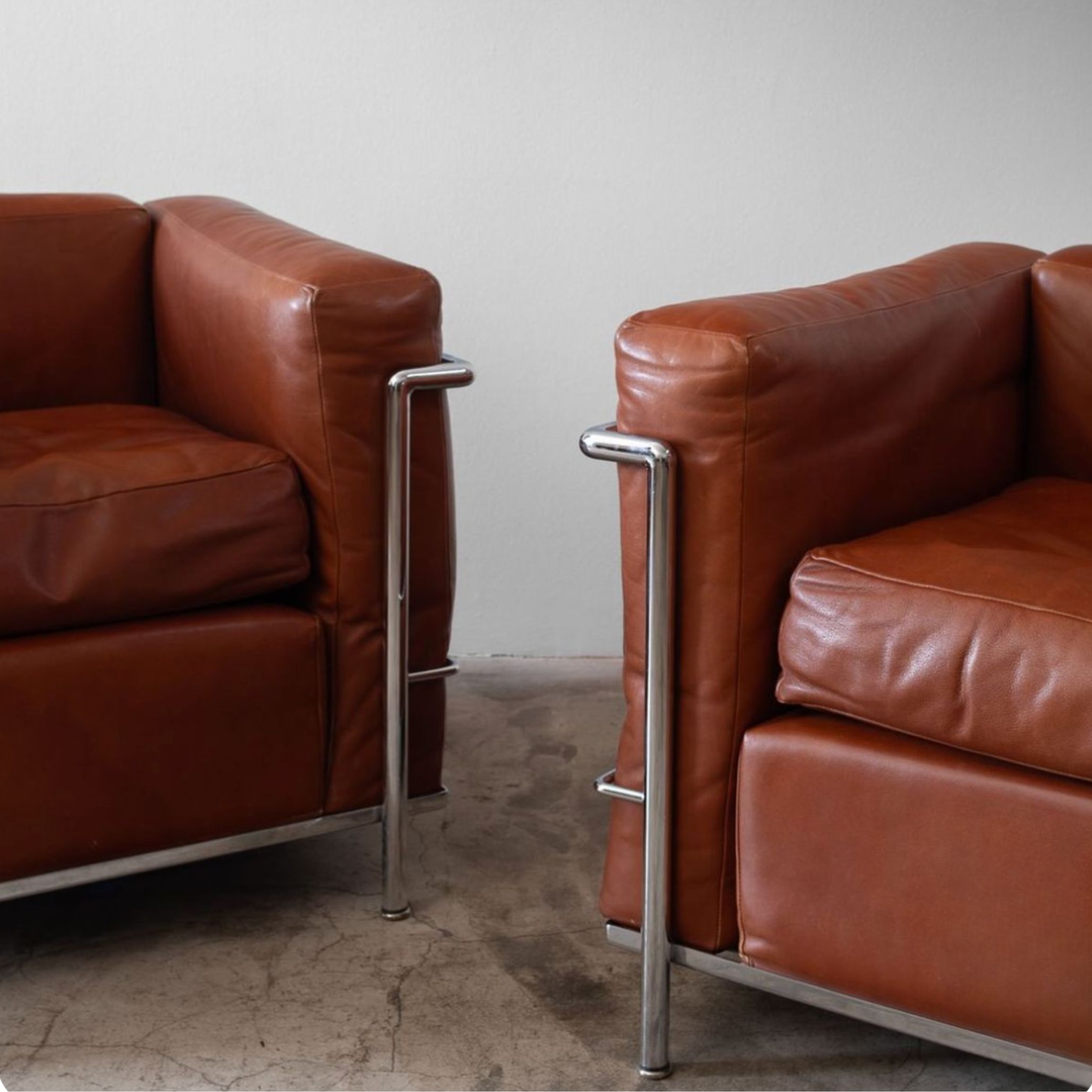A pair of LC2 Grand Confort chairs with a polished metal frame and structured leather cushions, illustrating the visual clarity that continues to influence luxurious furniture, guide the proportions of bespoke furniture, and define the clean geometry associated with contemporary furniture.