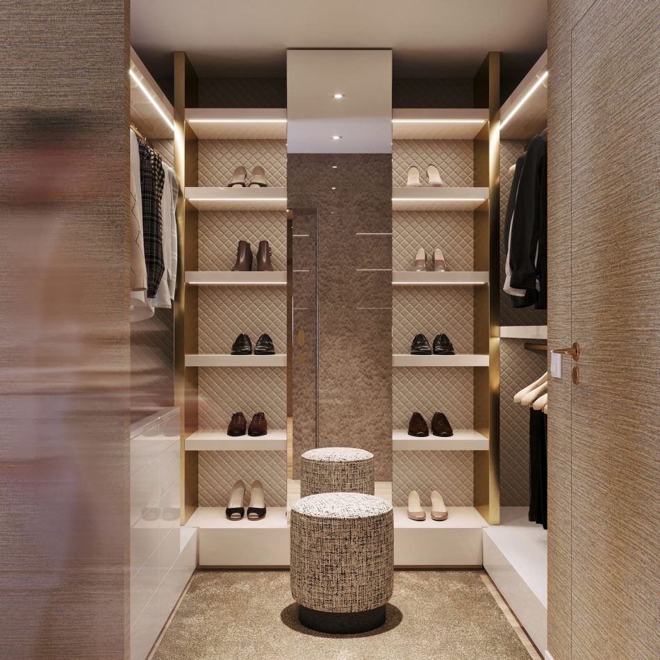 The walk‑in closet showcases quilted wall panels, illuminated shelving, and neatly arranged clothing and shoes. At the centre, the Sublime Stool introduces texture and comfort, enhancing the sense of order and warmth. The space reflects sophisticated luxury bedroom furniture, shaped by clean contemporary furniture, and enriched with subtle design details.