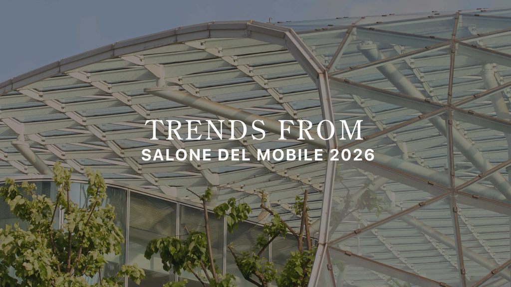 A geometric glass‑and‑steel canopy rises above lush greenery, framing the title “Trends from Salone del Mobile 2026.” The architectural transparency and natural elements echo this year’s themes,tactile materials, earthy palettes, organic forms, crafted details, and sculptural surfaces,capturing how Salone del Mobile 2026 moves beyond aesthetics toward more human, grounded, emotionally resonant design.