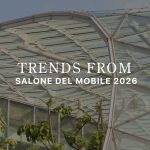 A geometric glass‑and‑steel canopy rises above lush greenery, framing the title “Trends from Salone del Mobile 2026.” The architectural transparency and natural elements echo this year’s themes,tactile materials, earthy palettes, organic forms, crafted details, and sculptural surfaces,capturing how Salone del Mobile 2026 moves beyond aesthetics toward more human, grounded, emotionally resonant design.