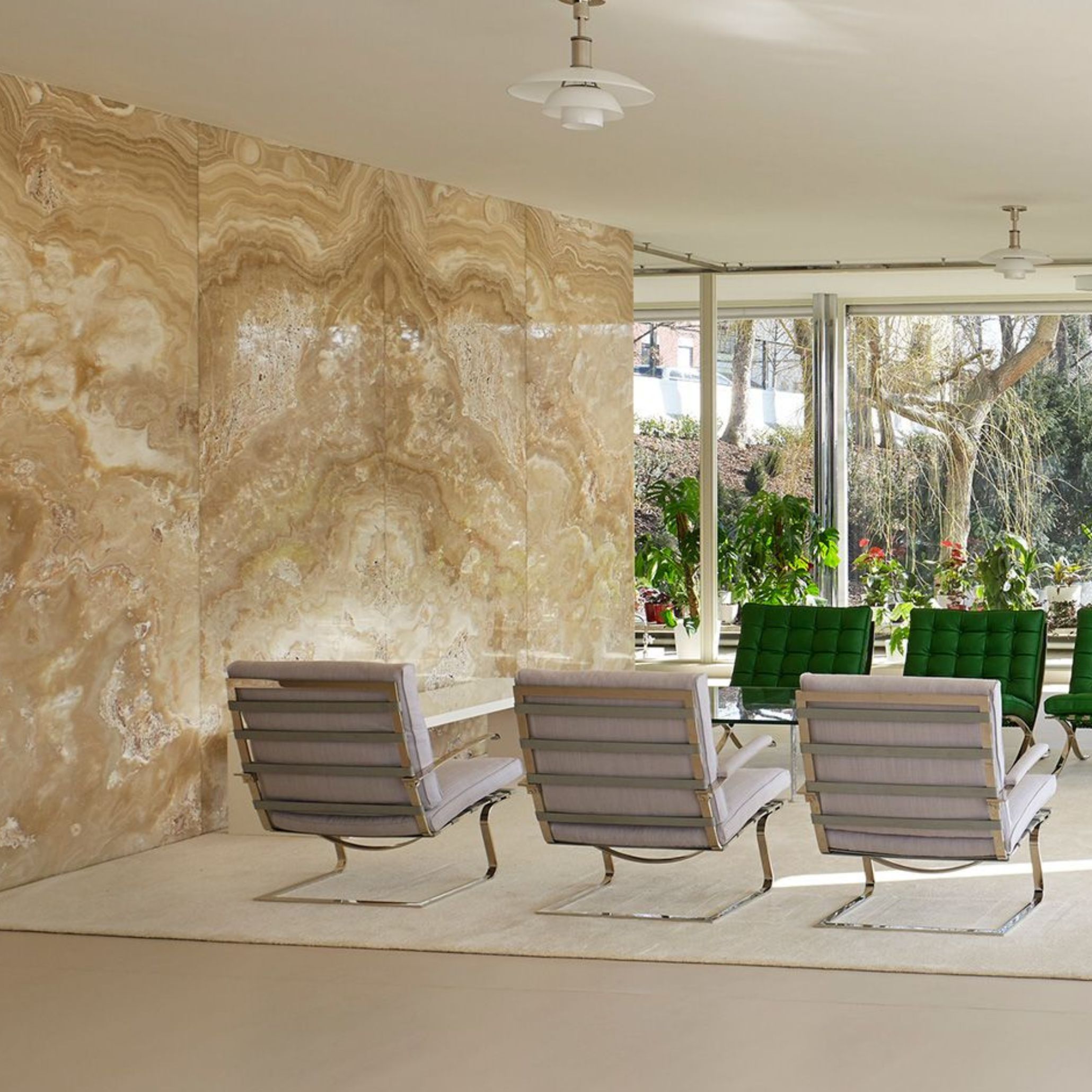 The main living space of Villa Tugendhat showcases the iconic onyx wall, chrome-framed chairs, and a low glass table set before floor‑to‑ceiling glazing that opens to the garden. The composition reflects luxury home furniture, sculptural design details, and the fluid openness central to living room architecture.