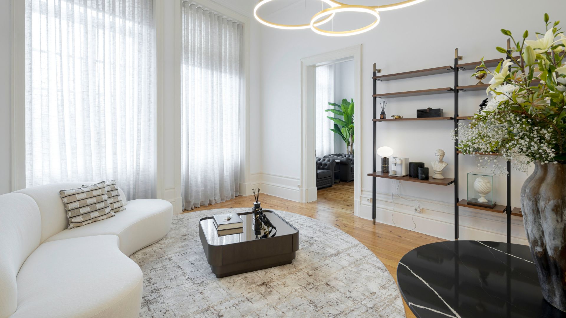 An elegant office setting features a confident editor seated at a sleek desk surrounded by framed photography, white florals, and tall windows that open to a city skyline, capturing the clarity and ambition of the Miranda Priestly aesthetic. The balanced composition blends modern office furniture, intentional design details, and aspirational interior design inspiration, reflecting a workspace where focus and authority shape every decision.