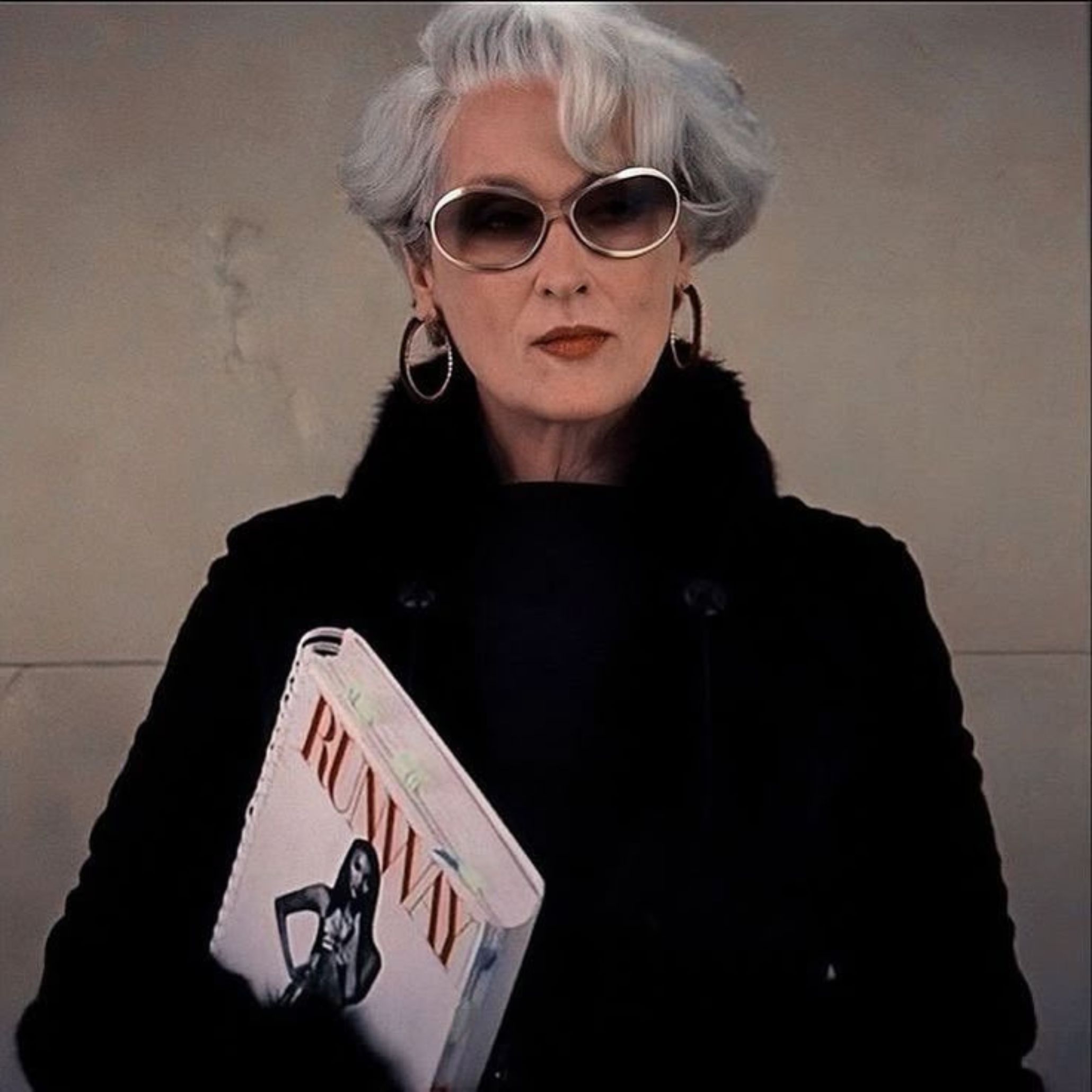 A poised figure styled in unmistakable Miranda Priestly fashion holds a Runway magazine, embodying the sharp authority and quiet power associated with her character. The composed expression, structured outerwear, and editorial attitude echo modern furniture restraint, elevated design details, and cinematic interior design inspiration.