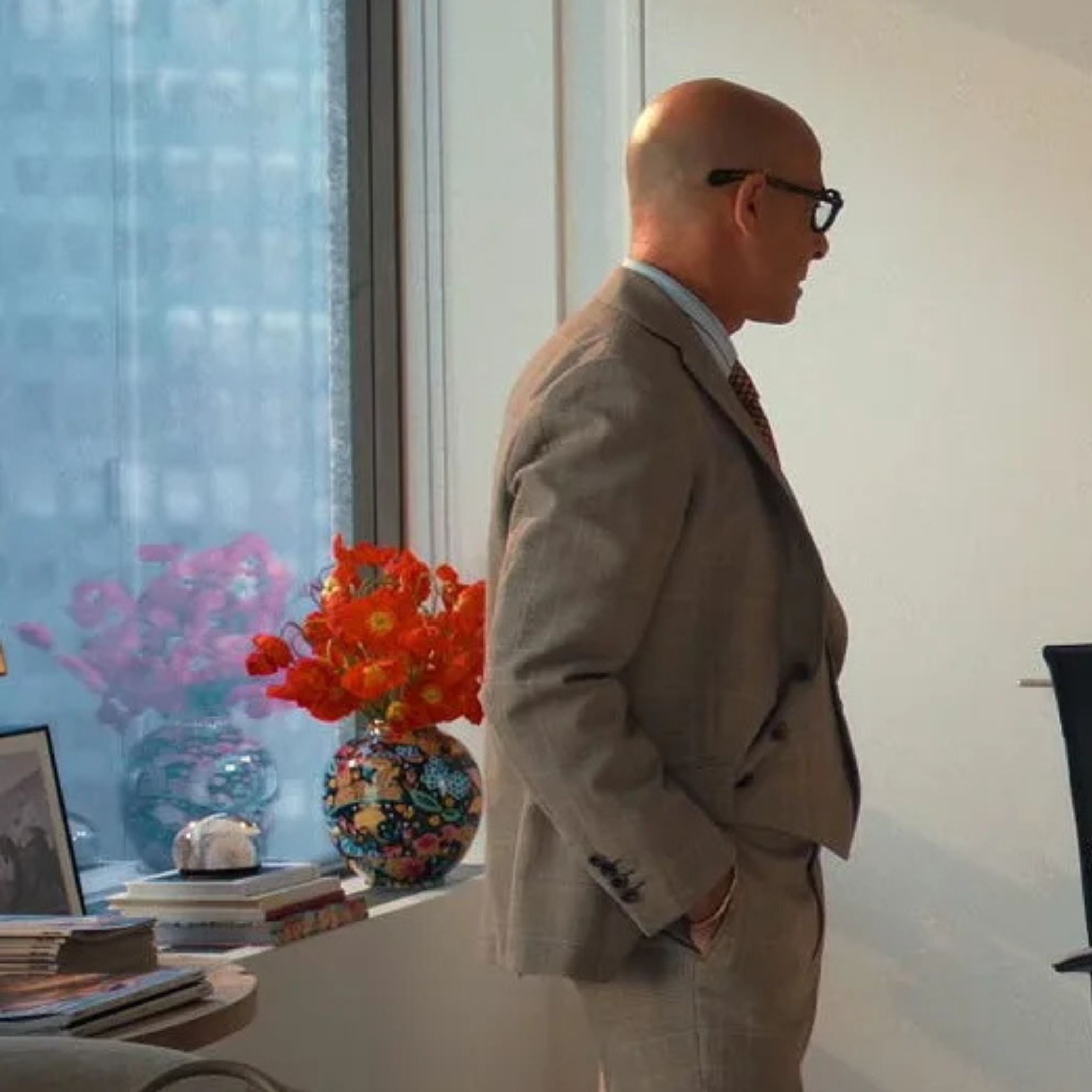 A bright vase of orange flowers sits on a windowsill beside stacked books and a framed photograph, bringing warmth to an otherwise structured office setting. The scene introduces gentle contrast through design details, complementing the clean lines of modern furniture and adding subtle interior design inspiration to the space.