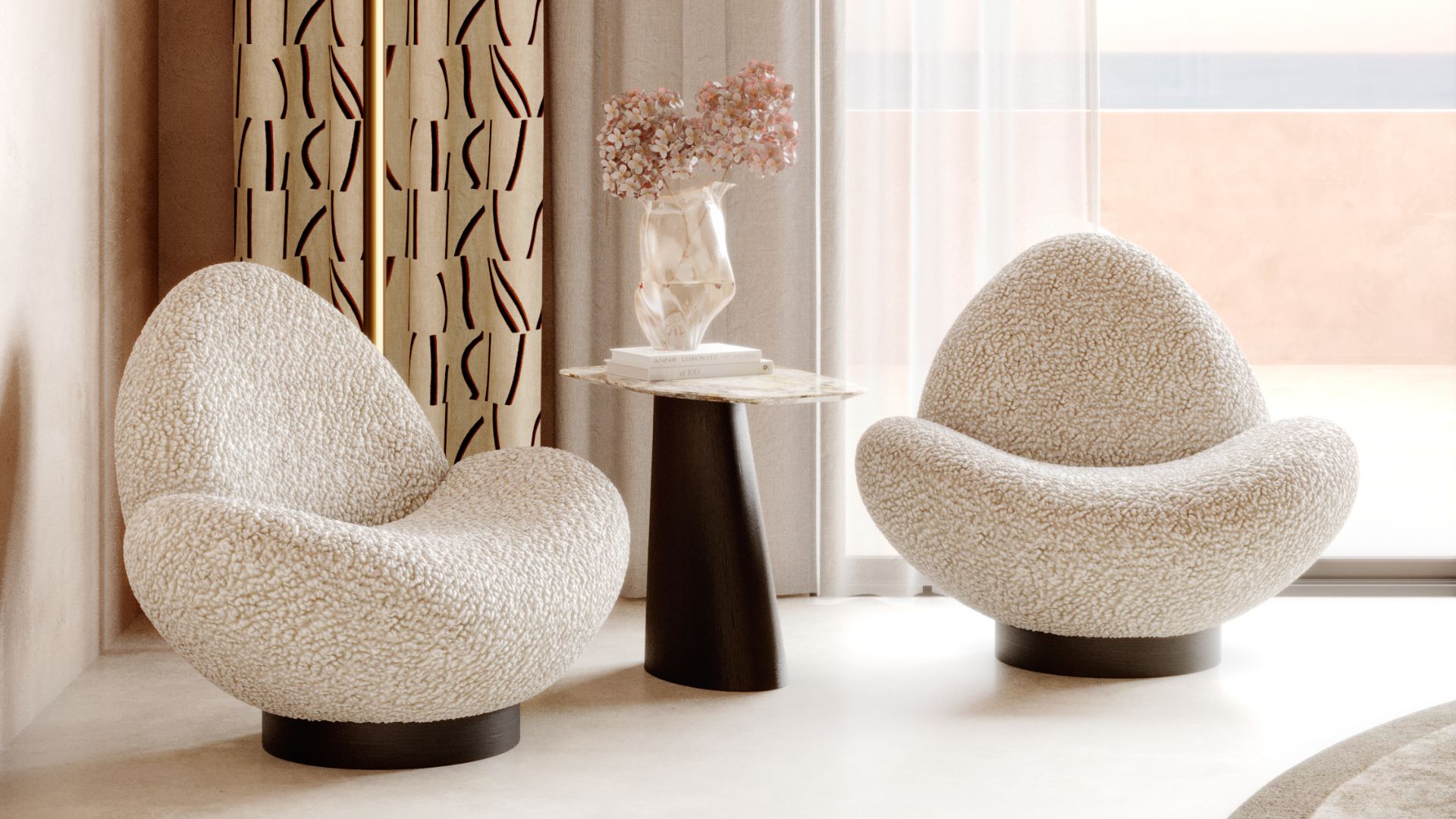 Two Stone Armchairs with rounded, sculptural silhouettes sit in a softly lit lounge, their textured upholstery echoing the smooth continuity of river‑shaped stone. A dark base side table with a light marble top anchors the composition, complemented by dried flowers and patterned curtains that filter natural light. The scene reflects expressive organic furniture, the quiet tactility of natural materials, and the sculptural clarity of contemporary design.