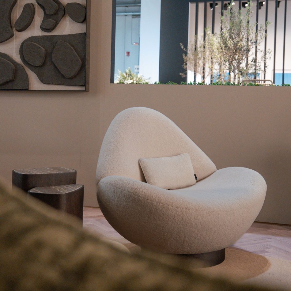A organic Stone Armchair in cream upholstery sits beside two dark wooden side tables, framed by a wall with raised stone‑like reliefs and an opening revealing greenery and vertical slats. The organic forms and natural textures highlight expressive luxury home furniture and handcrafted design details.
