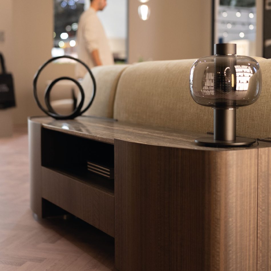 A Stone Low Console sits behind a beige upholstered sofa, styled with a black sculptural object and a dark glass lamp that casts a warm glow across the room. The clean lines and natural textures highlight refined living room furniture and contemporary design details within a calm, minimalist setting.