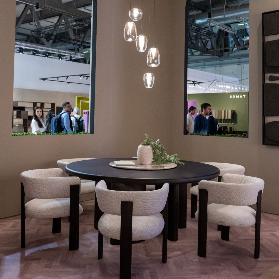 The Dolomites Round Dining Table is paired with six curved Dolomites Chairs in soft upholstery, illuminated by warm glass pendants above. The sculptural setting blends natural textures and refined materials, offering a contemporary expression of luxury dining room furniture and inviting dining room furniture inspiration within a modern interior.