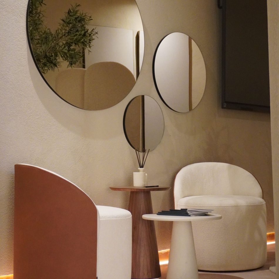 A cozy private corner features two rounded Elis Stools paired with the sculptural Olivier Side Table, styled with books and a diffuser. Overlapping circular mirrors and soft floor lighting create an intimate atmosphere defined by luxury home furniture and warm interior design inspiration.
