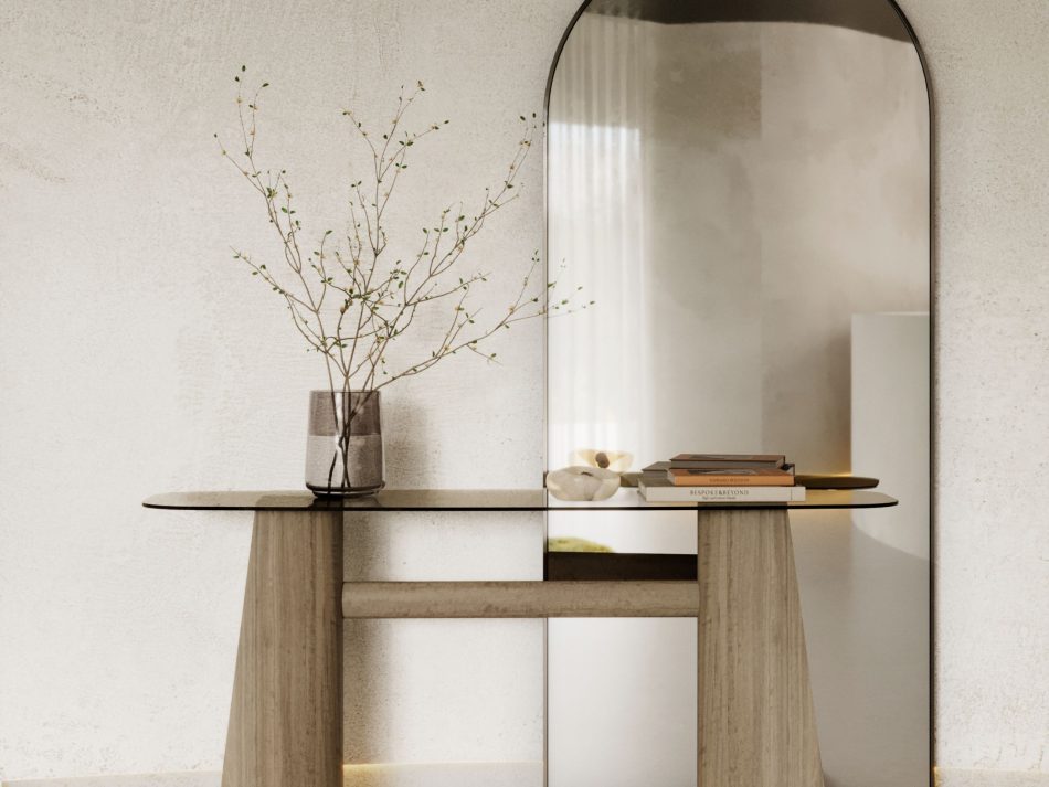 The entrance hall is softly illuminated, where the Toro Console rests against a textured wall, holding a simple arrangement of books and a glass vase with budding branches. Above it, the Her Mirror rises in a tall, arched silhouette, reflecting natural light and the greenery beyond. Clean lines, warm materials and gentle daylight shape a calm moment of arrival, expressing modern interior design, balanced contemporary interiors and sculptural architectural design.