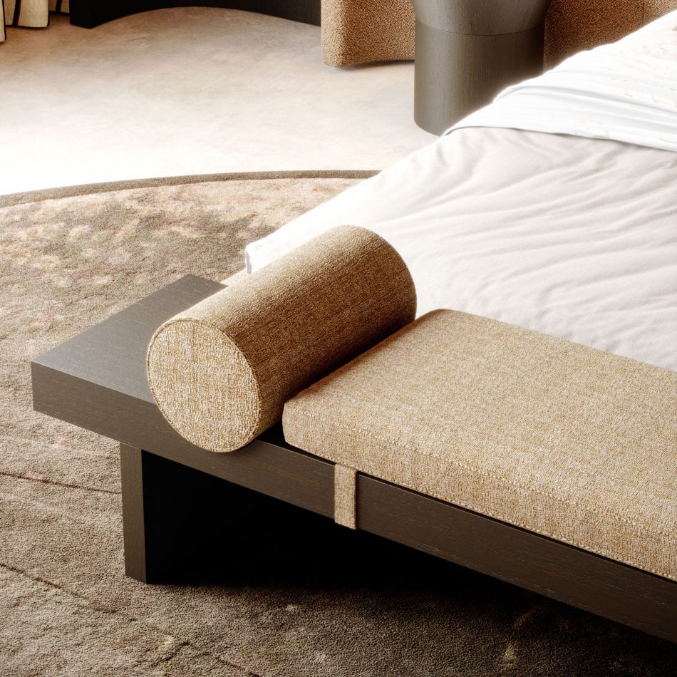 The Toro Bench anchors the foot of the bed, pairing a light upholstered cushion and cylindrical bolster with a grounded wooden structure. Surrounded by soft rugs, sculptural lamps, and warm tones, the space reflects luxury home furniture and contemporary interior design inspiration.