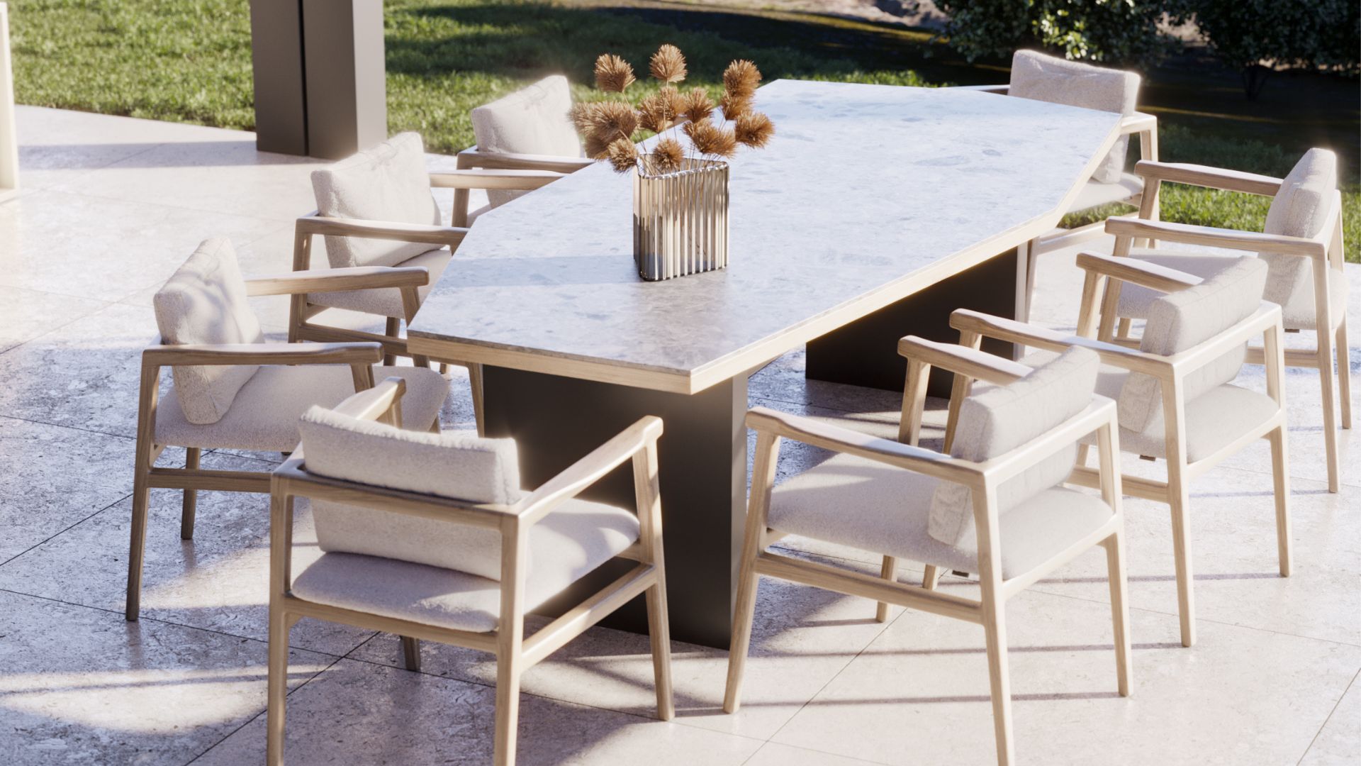 A modern alfresco dining setup featuring the Escarpa Dining Table with a marble top and dark metal base, surrounded by the Toro Chair in natural solid wood with thick cream upholstery cushions. The luxury dining table set is dressed with a single glass vase of dried botanicals, set on a stone terrace beside an open lawn. This contemporary dining table composition captures the relaxed elegance of the Italian Way, where bespoke dining room sophistication extends naturally into the outdoors.