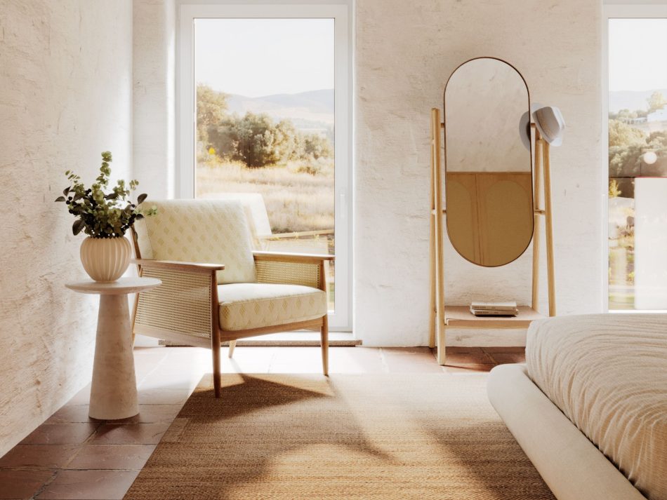 Sun-filled Comporta bedroom with whitewashed walls and terracotta tiles, featuring the Landform Mirror in natural solid wood and aged brass frame standing between two landscape-facing openings. A rattan armchair, olivier side table, and the Natur Bed complete a bespoke bedroom scene of mirror decor and luxury home furniture shaped by natural light and a quiet European summer sensibility.