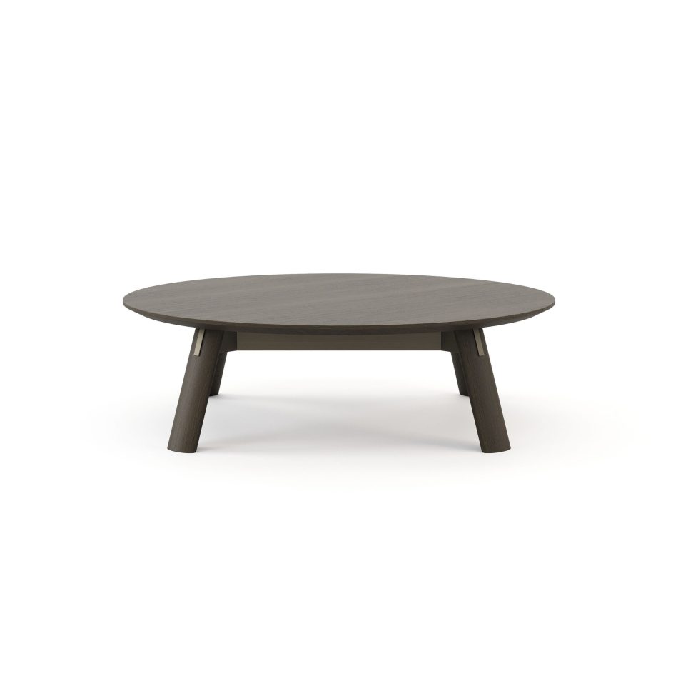 The Landform Coffee Table is shown front-on against a white background, its rounded oval top in dark oak resting on four angled legs joined by a slender stretcher with subtle silver-metal detailing. The gentle geometry and grounded stance reflect a luxury coffee table built on mid-century influence, where wood design carries the character of the piece.