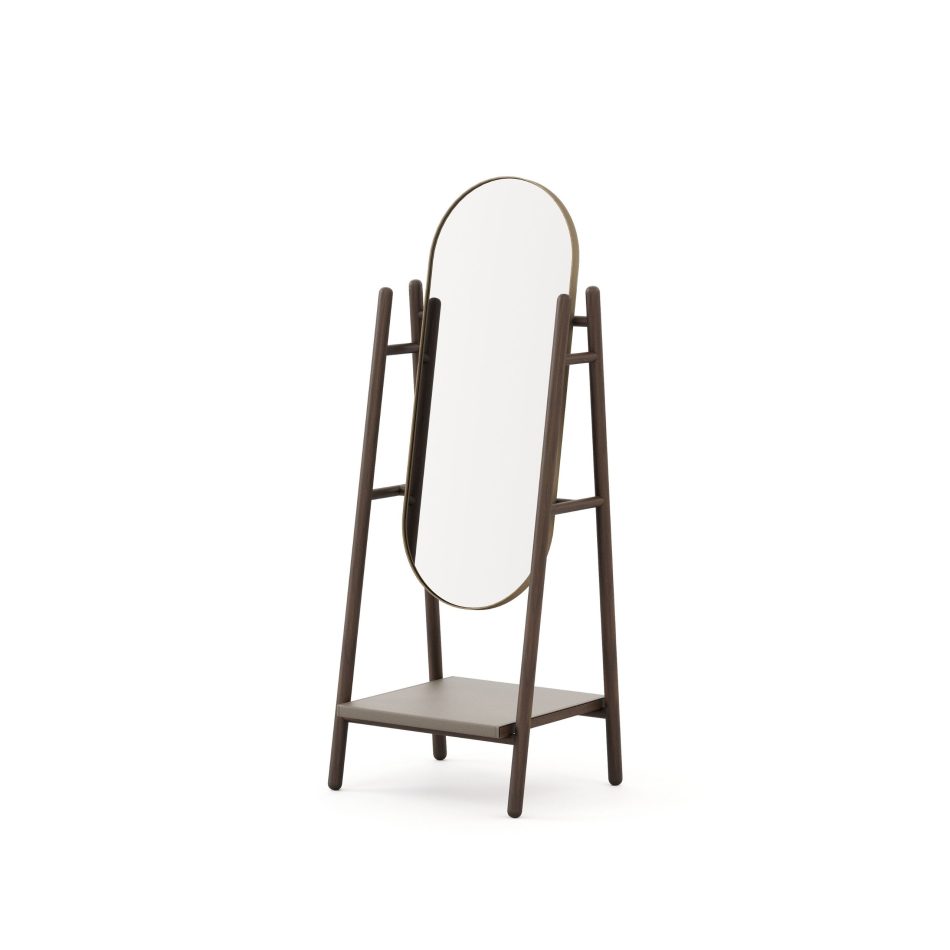 Landform Mirror seen from the side angle, revealing the angled dark wood design A-frame legs, the thin brass oval frame, and the low taupe shelf below. A piece of bedroom mirror long proportions and honest materiality, where duality and contrast between the warm metal frame and dark finest wood structure reflects the wabi-sabi spirit of the Landform collection.