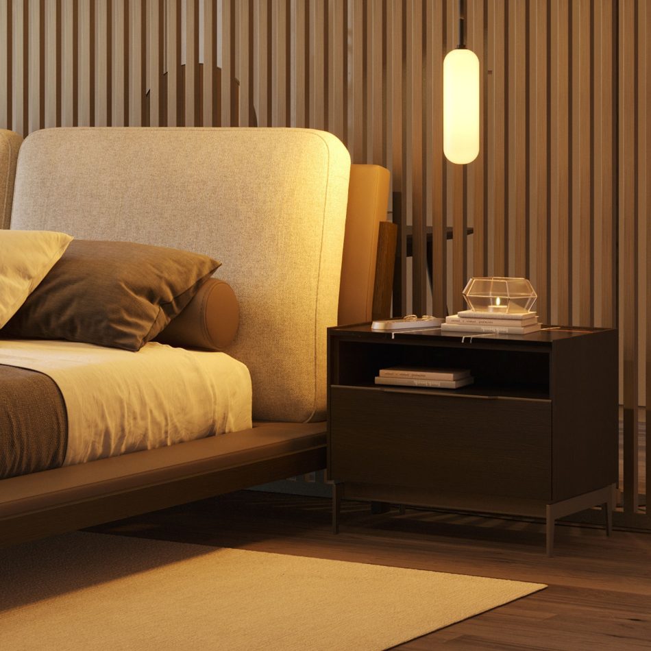 Moody, amber-lit bespoke bedroom featuring the Landform Night Table I in a dark finish, its wood design body and fine metal legs visible against warm wood flooring. A leather bench and travel bag rest at the foot of the bed, completing a scene of considered high end bedroom furniture where every piece earns its place without effort.
