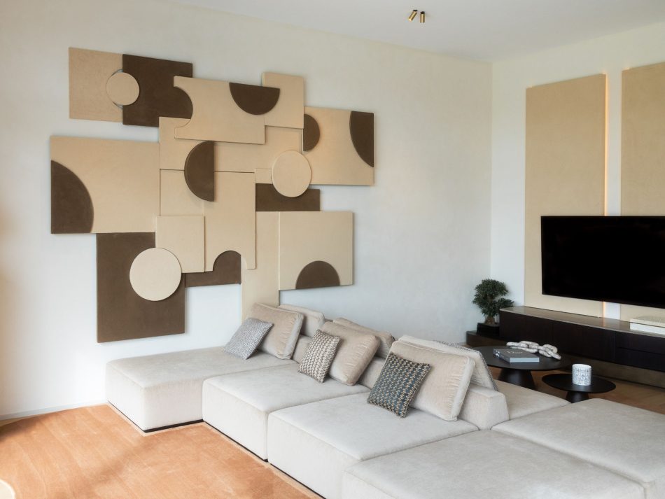 Contemporary living room featuring the Landform Modular Sofa in cream furniture upholstery fabric arranged in a bidirectional configuration, with a bespoke geometric artwork in sand and mocha tones covering the main wall. The Stone TV Cabinet in dark solid wood with a marble top closes the composition to the right, creating a balanced and considered bespoke living room of genuine architectural presence.