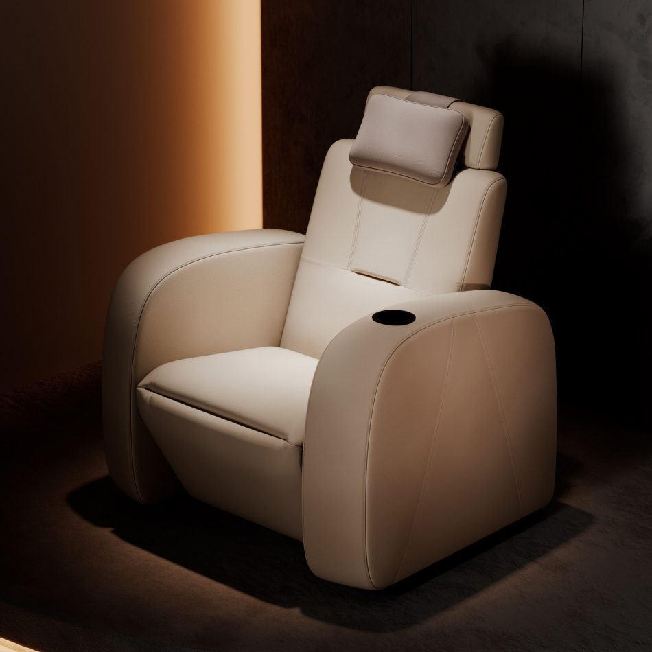 Lumière Cinema Armchair in cream leather upholstery view against a warm amber-lit interior, with the adjustable headrest raised and the integrated black cup holder visible on the armrest. A bespoke furniture piece of quiet sophistication, where minimalist design and precise proportions create an atmosphere of focused comfort for the discerning cinema space.