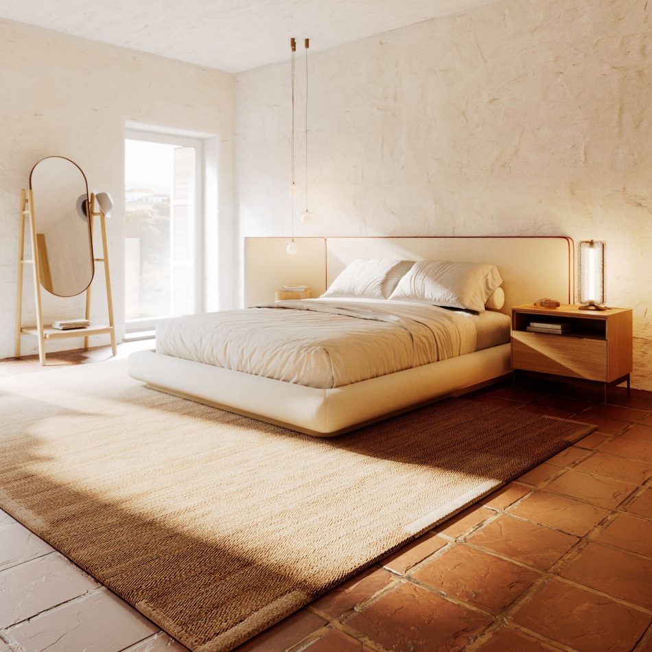 Sun-drenched bedroom with whitewashed plaster walls and terracotta floor tiles, centred on the Natur Bed in warm cream furniture upholstery fabric with a wide asymmetric headboard edged in a terracotta piping detail. The Landform Night Table I in natural oak flanks the bed to the right, while a freestanding mirror on a timber frame adds depth to the left. A complete scene of luxury bedroom furniture and interior design inspiration rooted in organic materials and natural light.