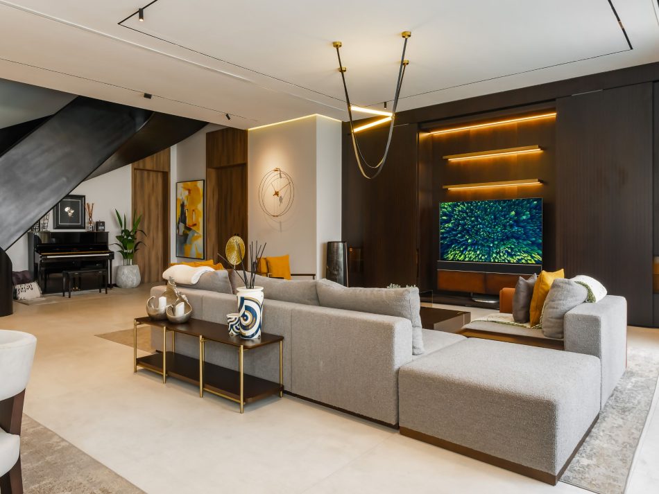 The living area centres on the His Sofa in grey bouclé, with the Fortune Coffee Table in dark wood and polished brass at its core. A backlit timber panel frames the television wall, creating duality and contrast against the room's cooler tones. The Her Low Console behind the sofa adds a layer of quiet order to this bespoke living room, where modern luxury furniture feels inseparable from its surroundings.