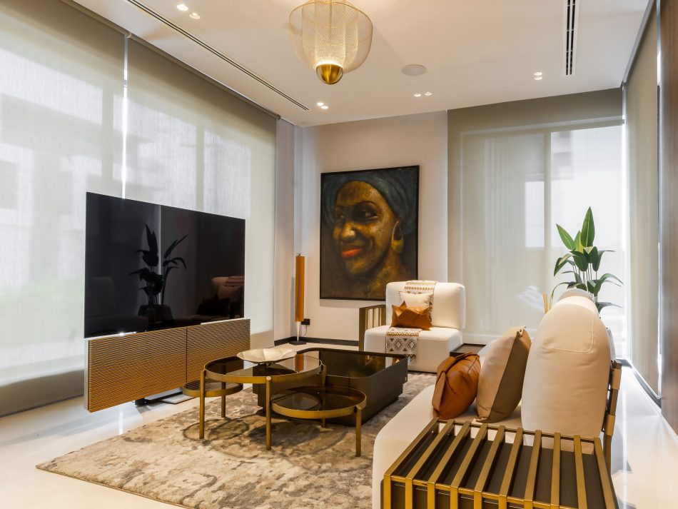 A private lounge on the bedroom floor arranged around the Her Sofa in neutral upholstery, with the Her Coffee Table in brushed bronze and smoked glass at its centre. The His Coffee Table in dark wood introduces duality and contrast, grounded by a portrait painting that gives the room a personal, unhurried character. A ribbed timber tv cabinet and gold-plated brass ceiling pendant complete a bespoke living room that feels like an extension of the private quarters rather than a formal space.