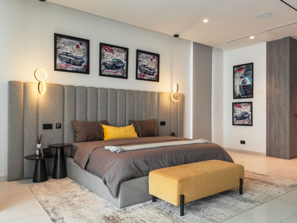 A teenager's bedroom where the Milan Bed's tall channelled headboard in grey upholstery anchors a room full of graphic energy. England-inspired automotive artwork lines the walls, balanced by the ochre Terra Bench in velvet furniture at the foot of the bed. The Olivier Side Tables keep the layout clean, delivering high end bedroom furniture with personality and without sacrificing the composure that runs through the whole residence.