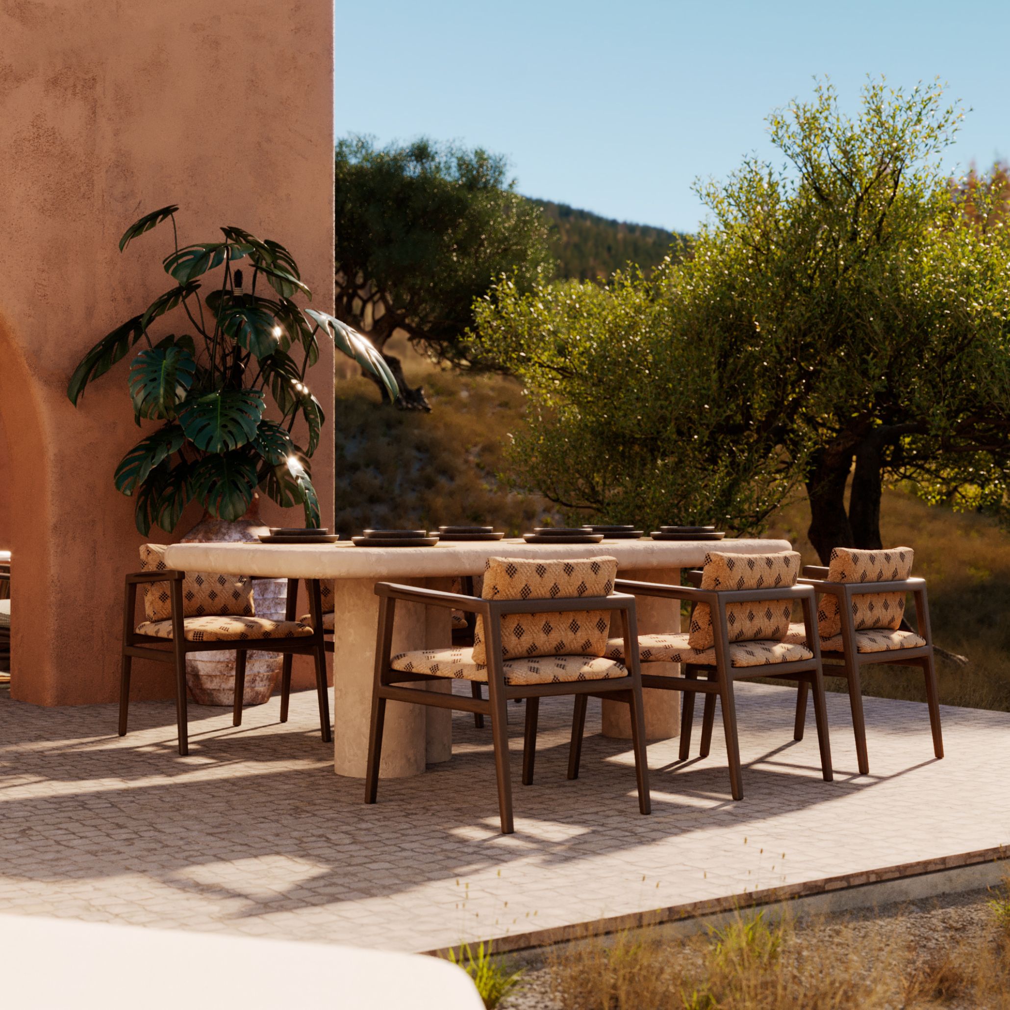 The Natur Dining Table paired with woven Toro Chair seating on a terracotta-hued terrace, set with ceramic dishware and a monstera plant, framed by hillside greenery, an inviting alfresco dining area for slow summer gatherings.