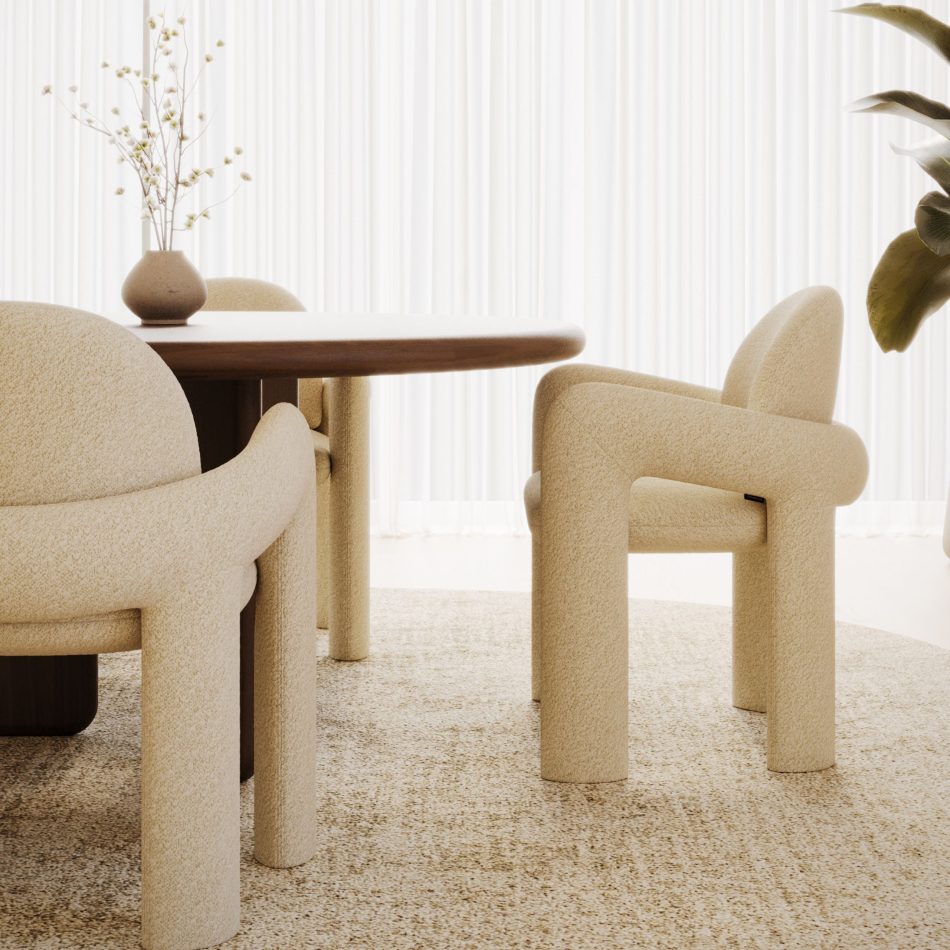 A warm, sunlit dining corner where a round walnut table is surrounded by Stone Chairs upholstered in soft cream bouclé, their arched backs and thick cylindrical legs catching the light against sheer curtains and a speckled beige rug. The chair's rounded arms and continuous organic contemporary form stand out as the focal point of living room furniture styling, with a stoneware vase of white blossoms adding a natural, understated finish.
