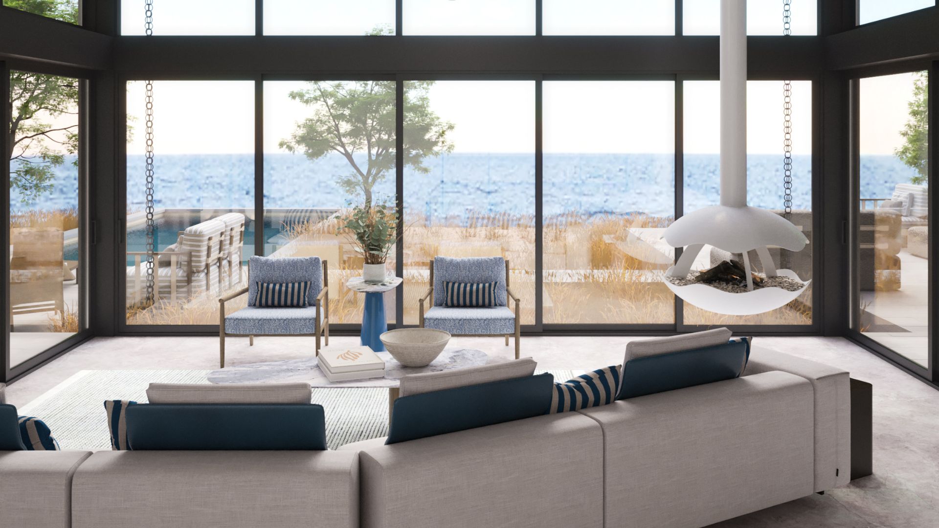A coastal living room with a striped navy-and-cream sectional sofa and blue textured armchairs facing floor-to-ceiling glass overlooking the sea, an example of luxury living room furniture and modern furniture in living room design inspired by Riviera Lines.