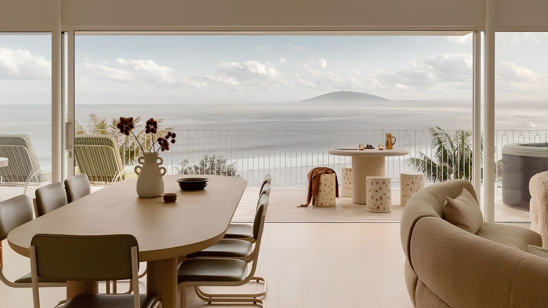 An open dining and living area with sage-striped chairs and matching lounge chairs on the terrace, framed by floor-to-ceiling windows overlooking the sea and distant hills, an example of luxury dining room furniture reflecting Riviera Lines stripes design.