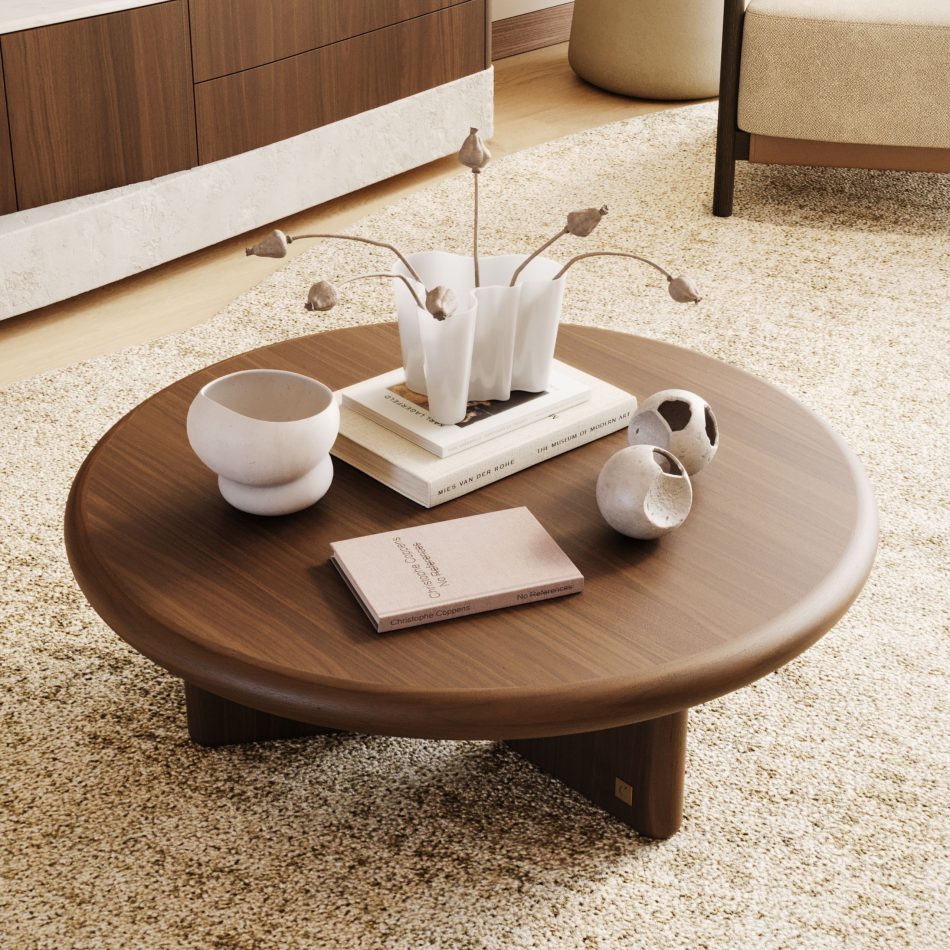 The Foz Coffee Table sits on a light textured rug, its wooden top arranged with ceramic pieces, dried stems, and stacked books. A wooden cabinet and a beige chair complete the warm, minimalist setting, where natural materials shape a calm interior. The vignette reflects thoughtful home furniture in the composition, sculptural design details in the objects, soft living room furniture in the layout, and modern interior design inspiration in the overall feel.