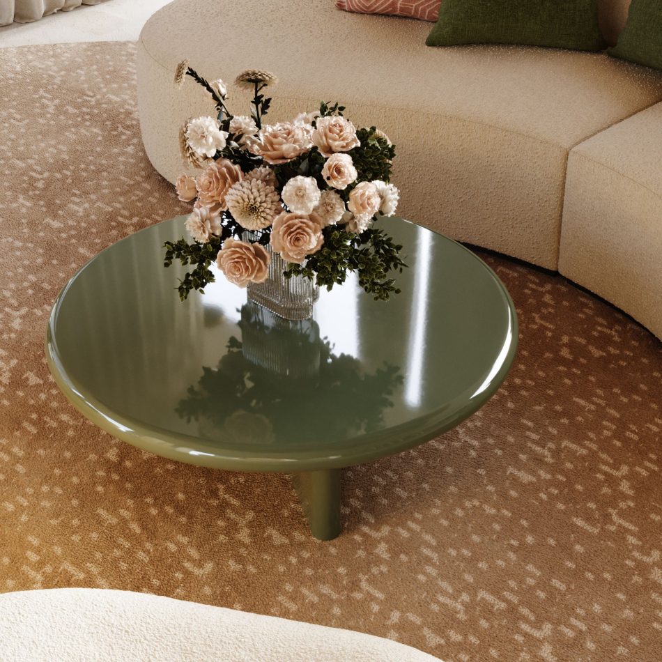 The Foz Coffee Table in glossy lacquer appears within a serene living room, its smooth green surface holding a delicate bouquet that softens the contemporary setting. A curved textured sofa surrounds the table, blending crafted home furniture with muted tones that enhance the room’s calm atmosphere. The composition highlights sculptural living room furniture, understated design details, and modern luxury home furniture that shape a sophisticated interior.
