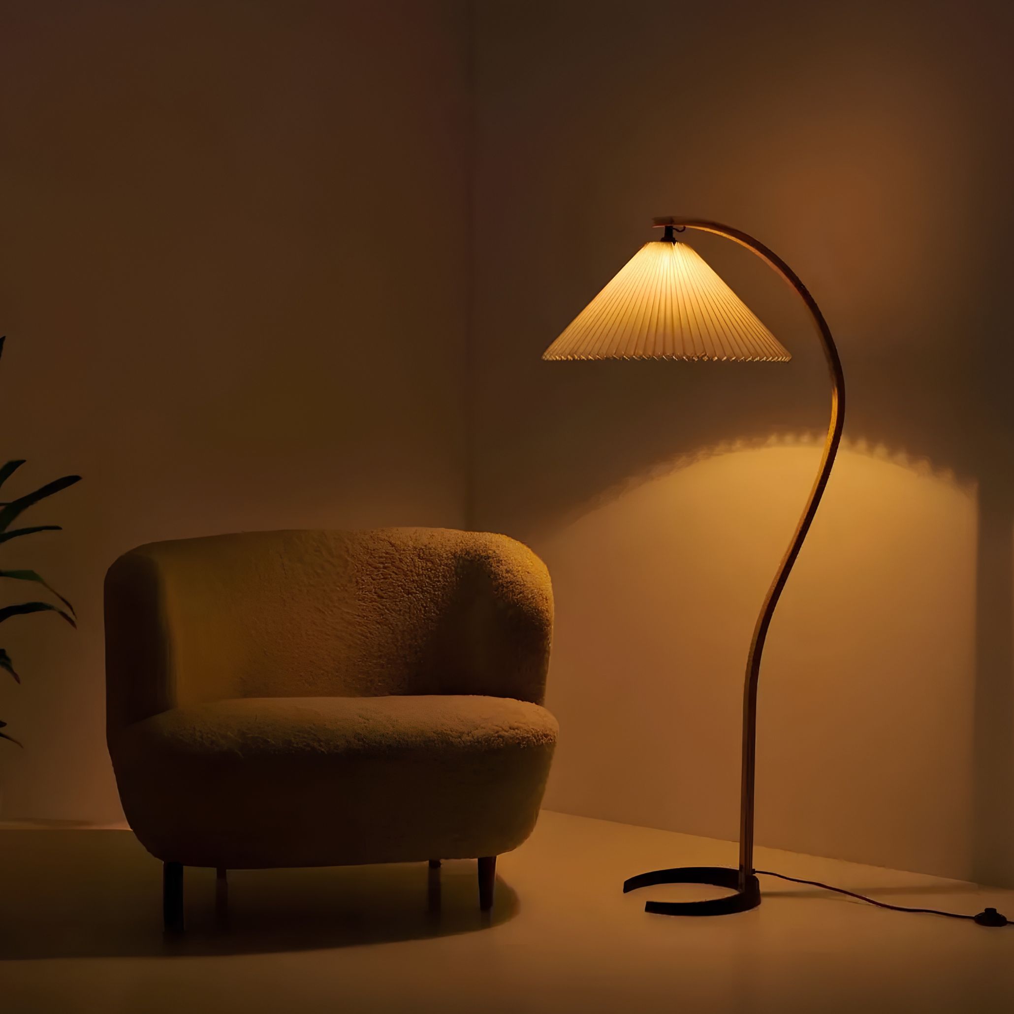 Cozy living room ideas showcasing a curved floor lamp casting a gentle glow next to an armchair, embodying warm minimalist interior design for the season.