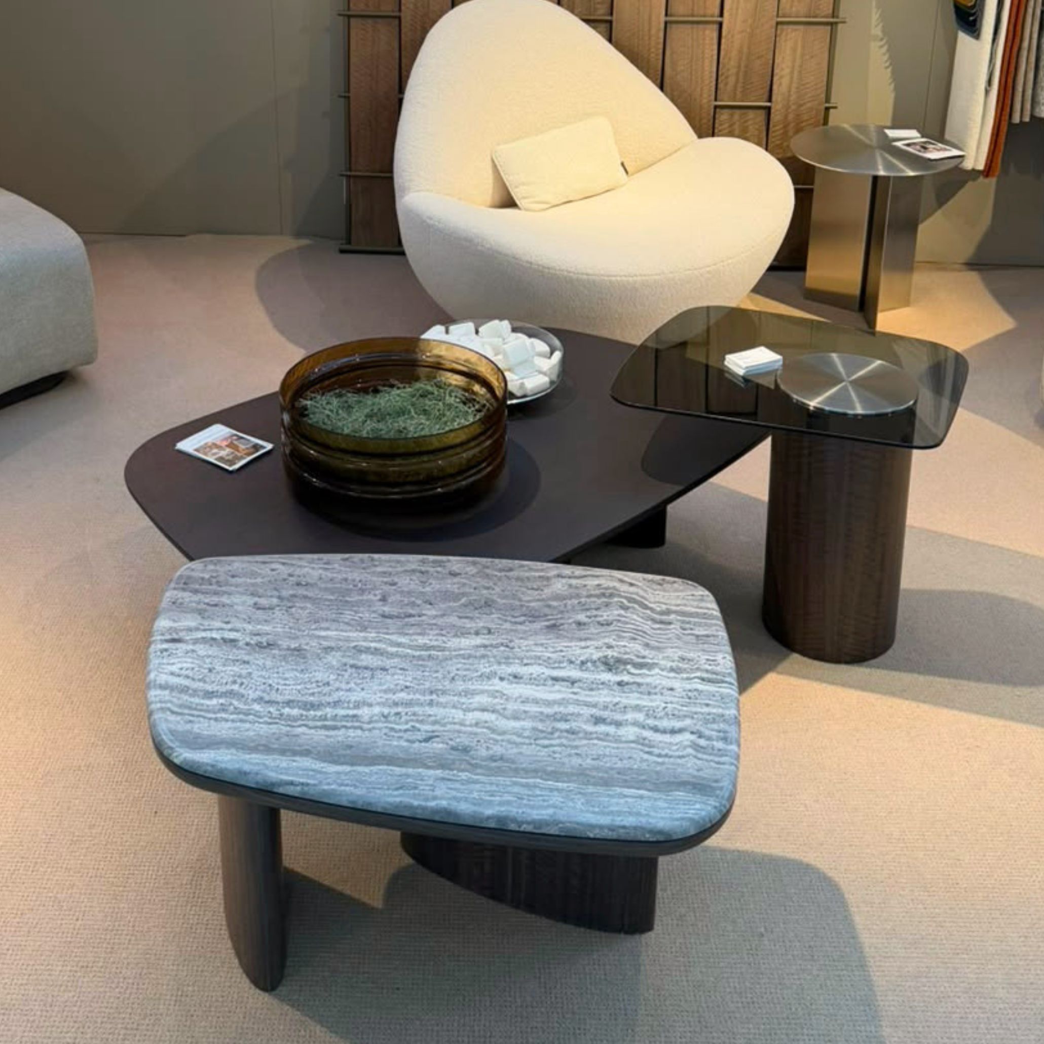 Dolomites Coffee Table arranged inside Stylish Club’s Decorex 2026 stand alongside a plush rounded armchair. Featuring an asymmetric interplay of natural stone, dark wood, and tinted glass, this setup offers living room inspiration through elevated design details and modern furniture for living room spaces.
