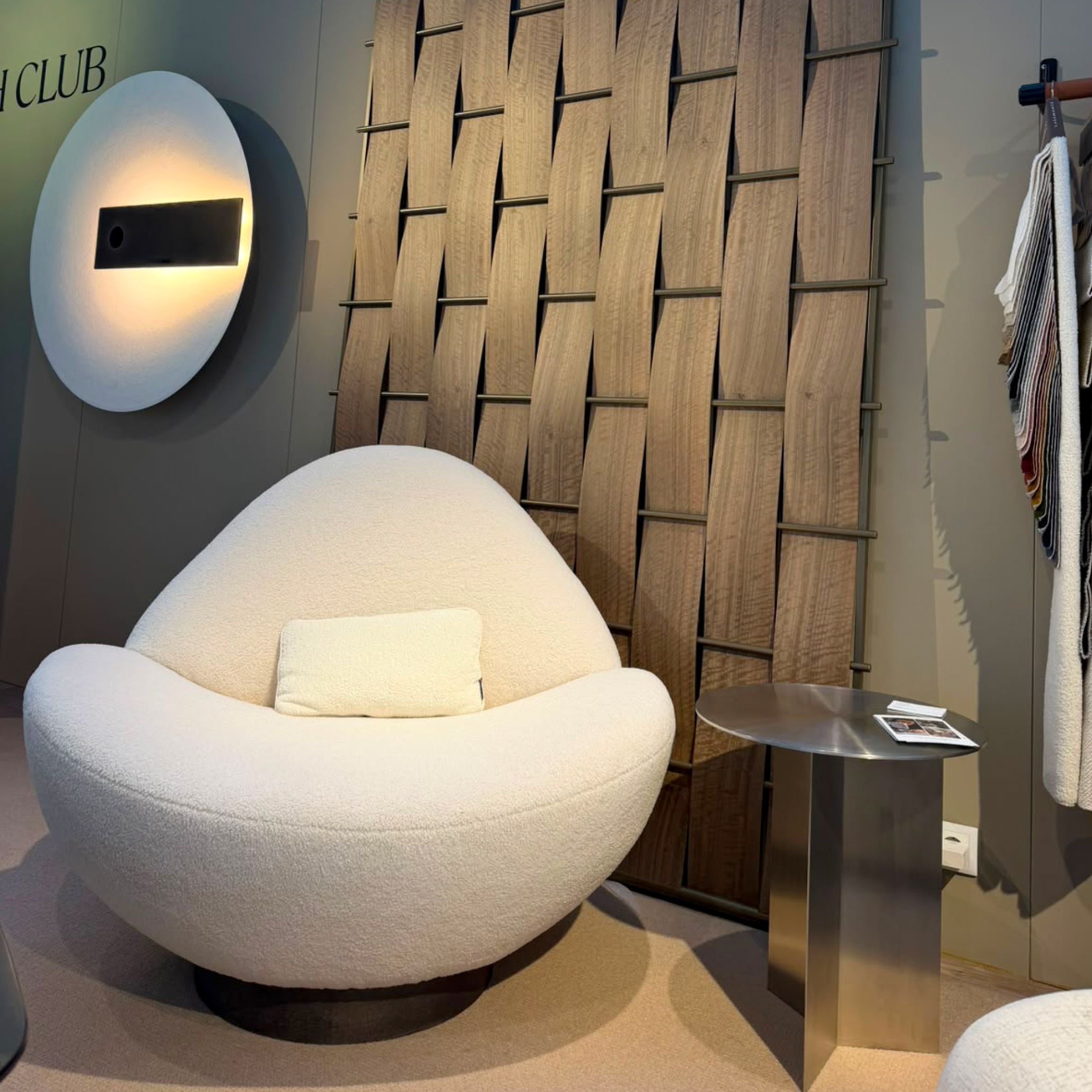 The Elis Side Table placed alongside the organic Stone Armchair at Stylish Club's Decorex 2026 exhibition stand, set against a woven wood panel wall. The architectural metal form offers striking living room inspiration, subtle harsh and strict lines, and elevated side tables for contemporary lounge areas.