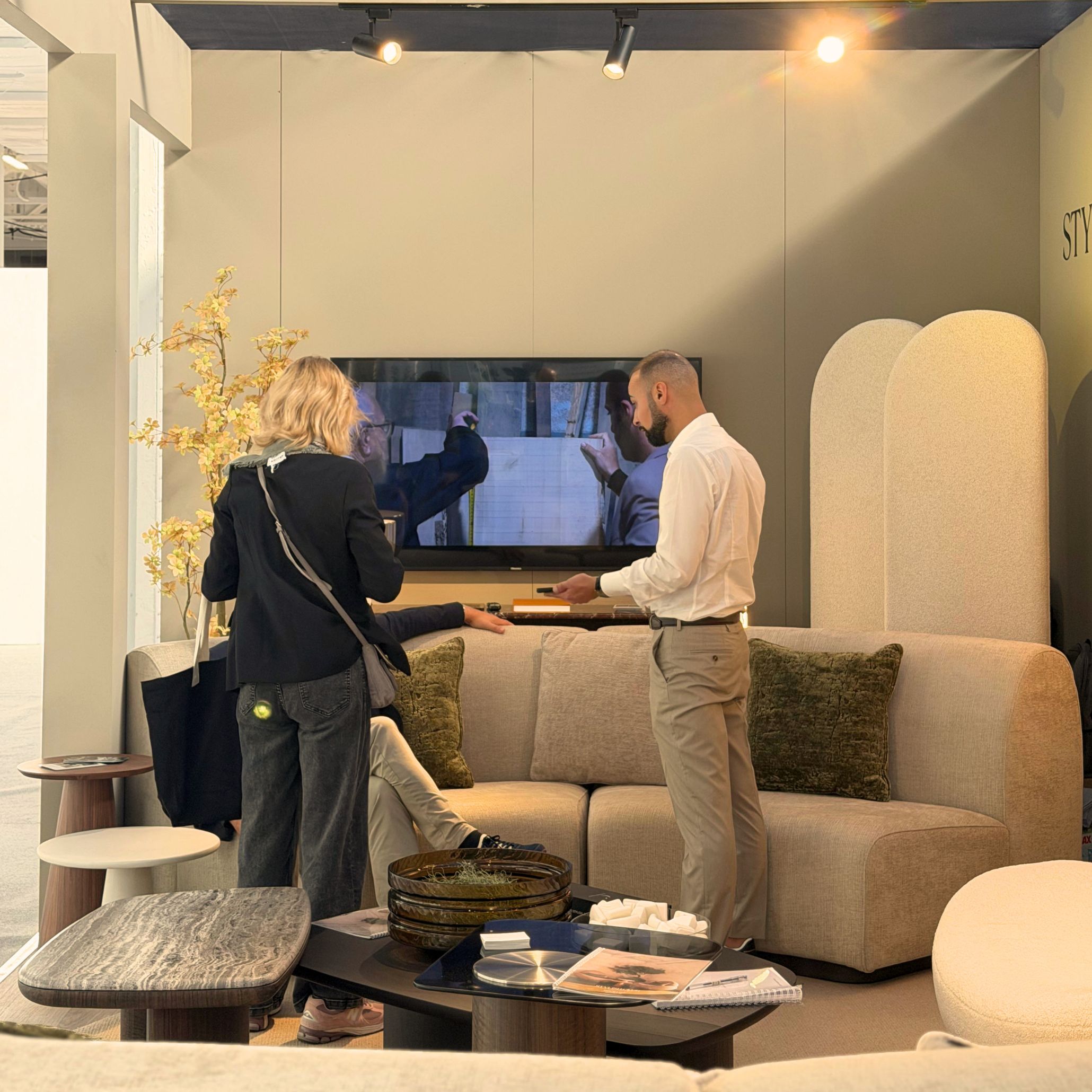 Visitors and designers in conversation with a Stylish Club representative at Decorex 2026 around the Stone Sofa and low center tables. The interactive setting provides rich interior design inspiration, showcasing custom furniture and modern living room furniture in a collaborative environment.